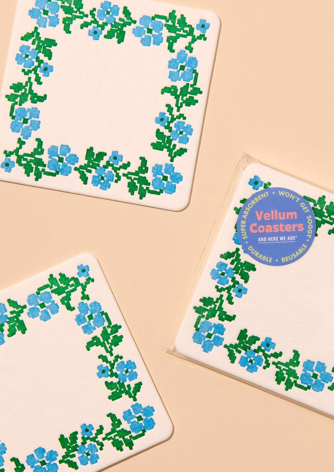 A set of paper coasters with blue and green needlepoint floral pattern.