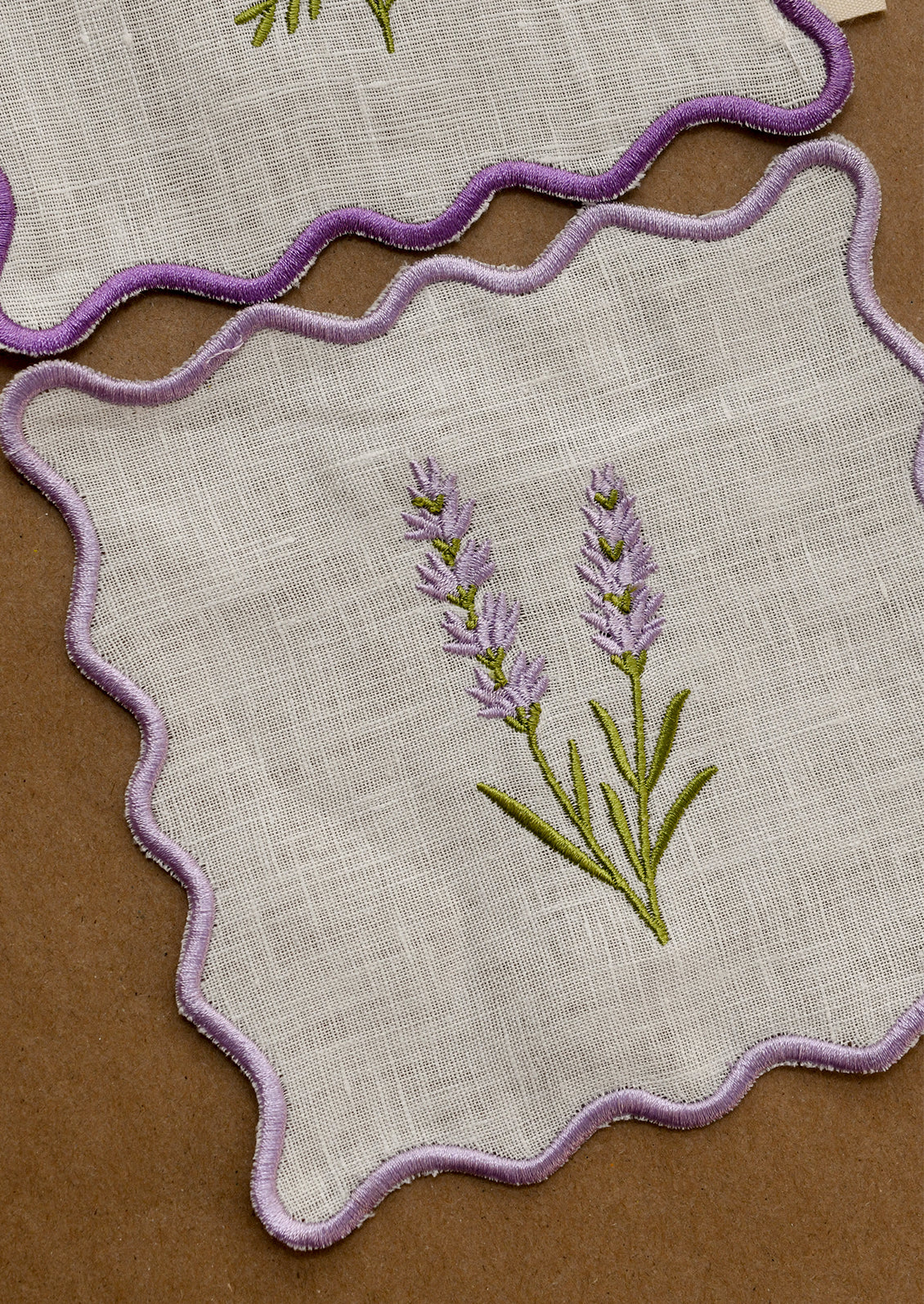 A cocktail napkin with scalloped purple edges and lavender sprig embroidery.