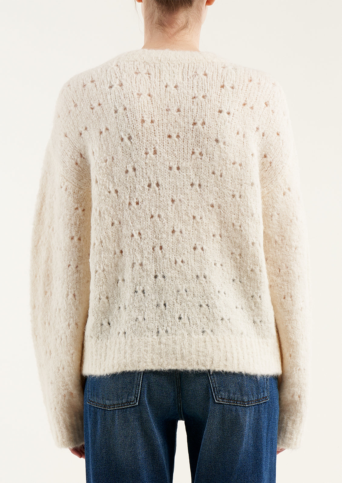 A woman wearing a fuzzy cream colored sweater with double birdseye cutout pattern throughout.