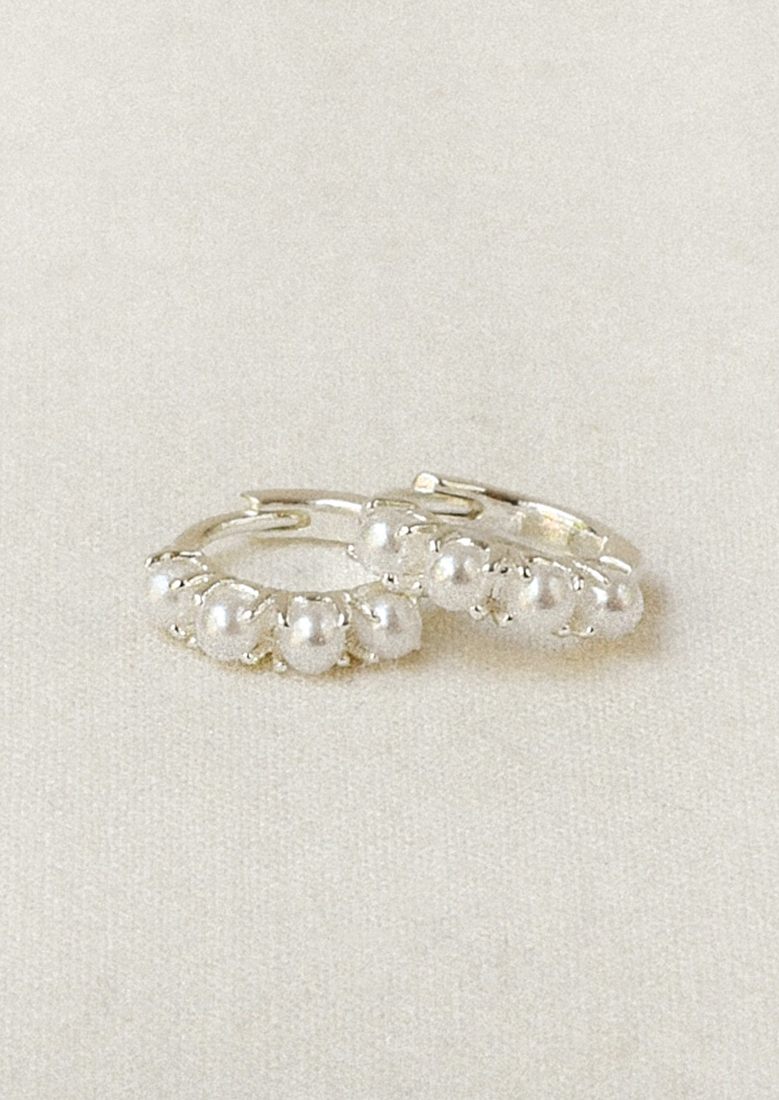 A pair of sterling silver huggie hoop earrings adorned with imitation pearls