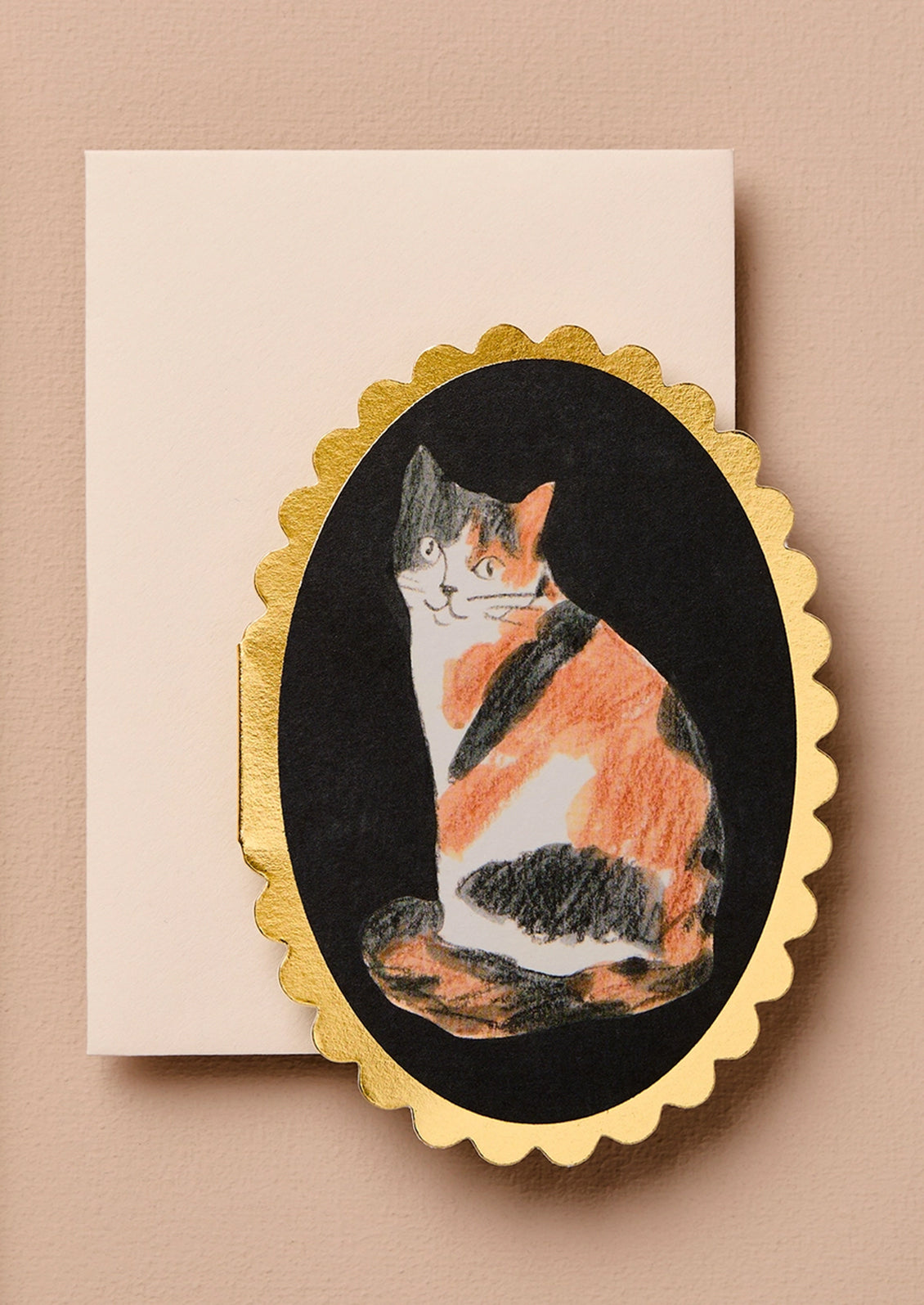 An oval-shaped mini greeting card featuring an illustration of a calico cat illustration on a black background with a gold scalloped border.