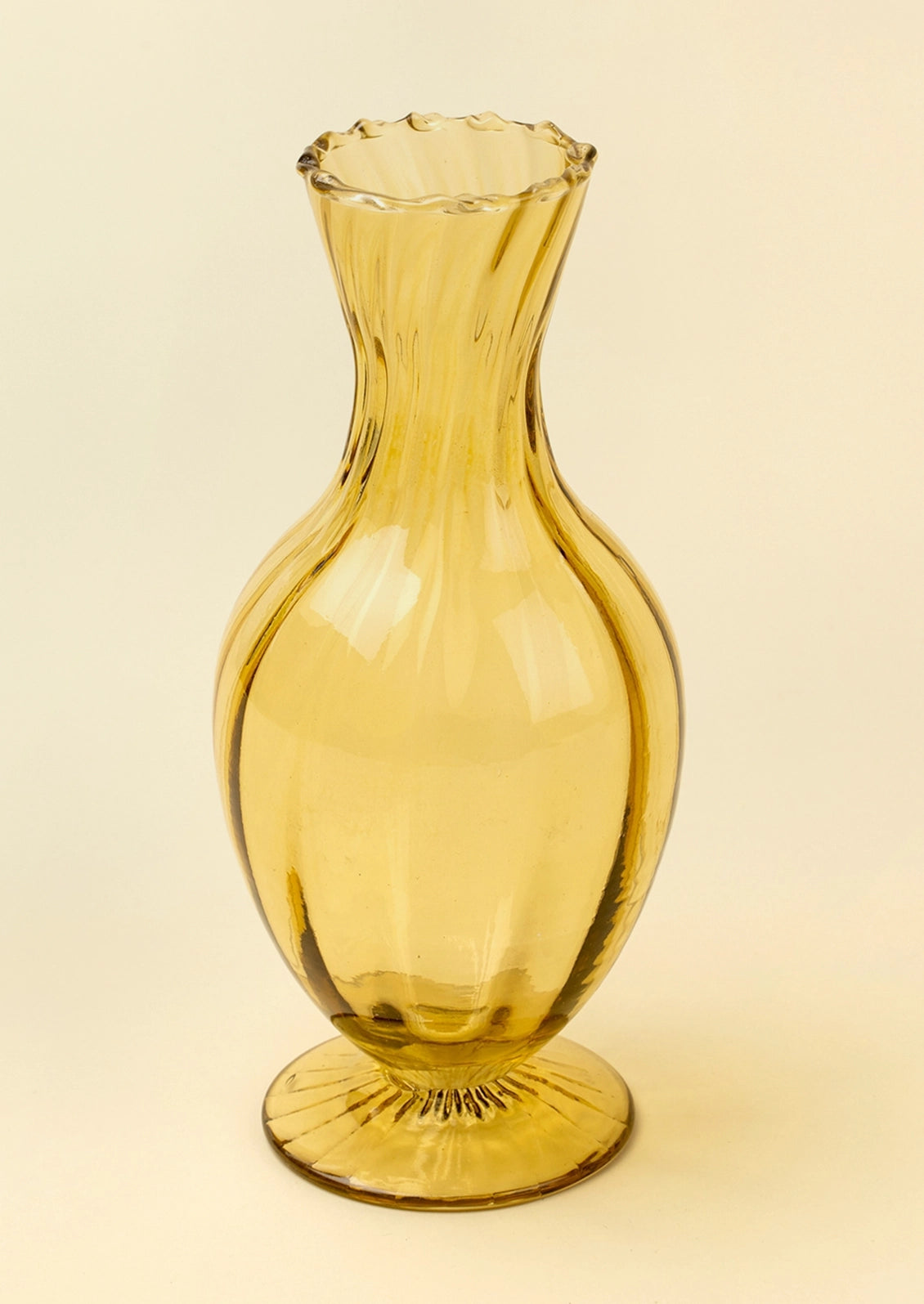 A translucent amber yellow glass vase with a flared scalloped rim and a fluted circular base, shown on a plain light beige background.