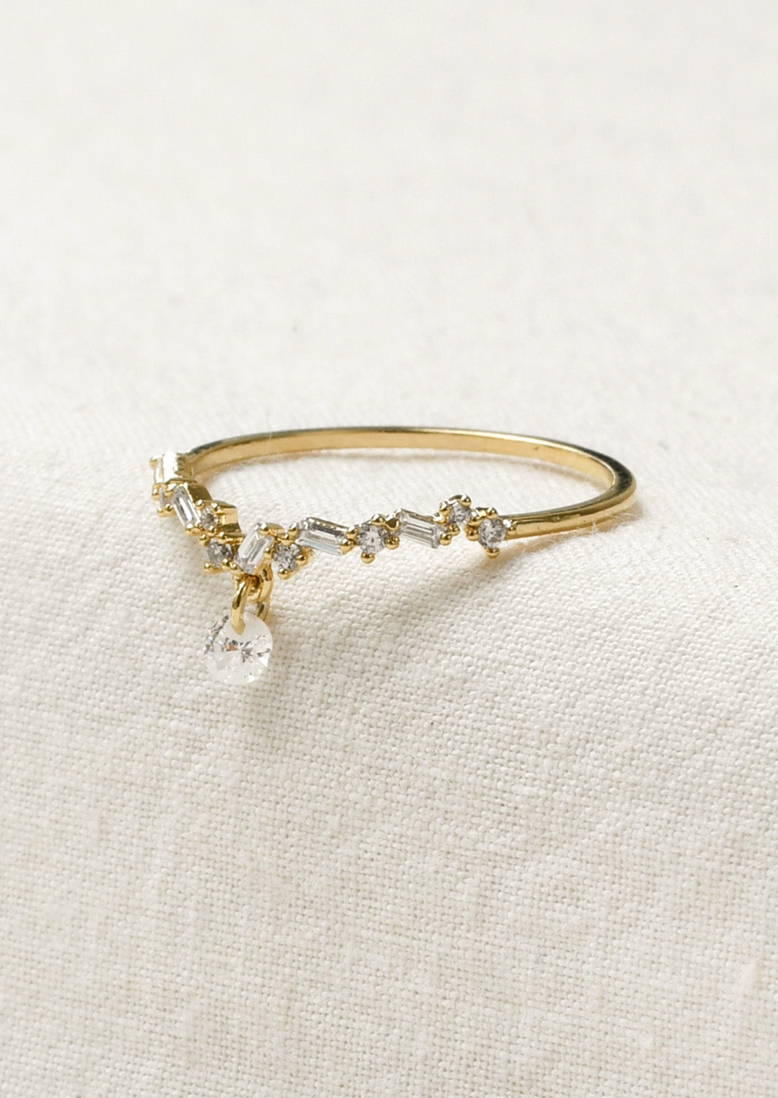 A gold ring with a dipped v design adorned with small variously shaped cubic zirconia and a large round one dangling from the center.
