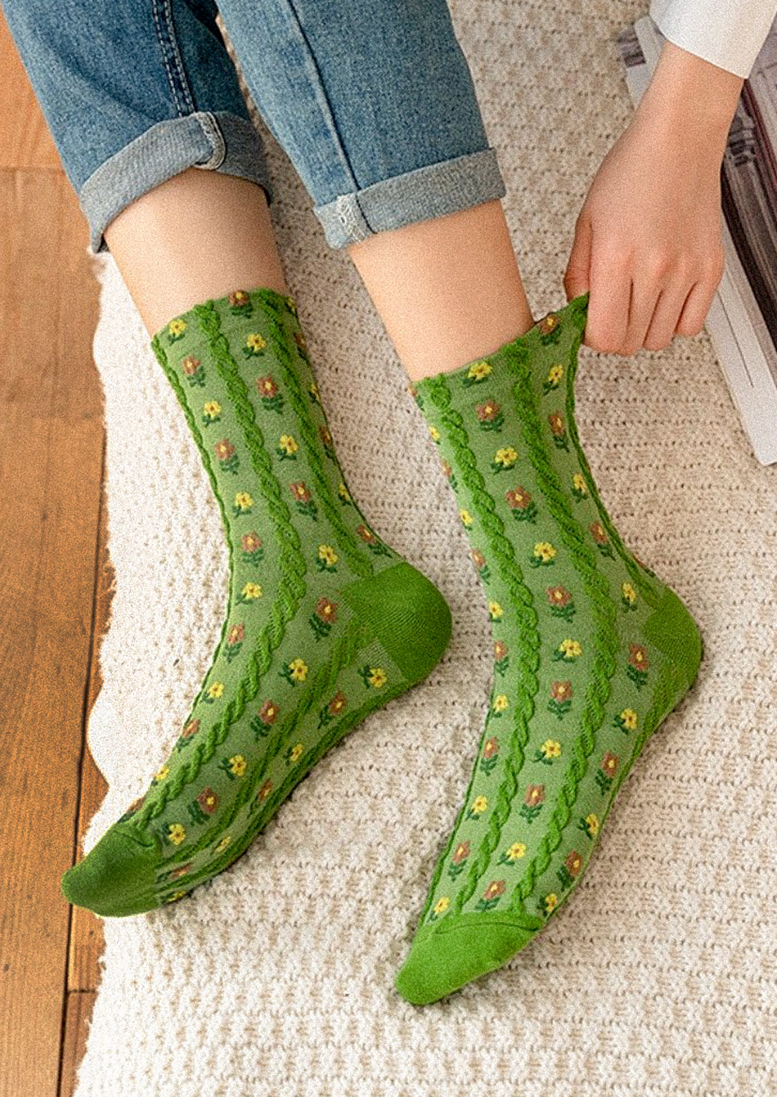 A person sitting on a bed and wearing a pair of green crew socks with small brown and yellow flowers throughout.