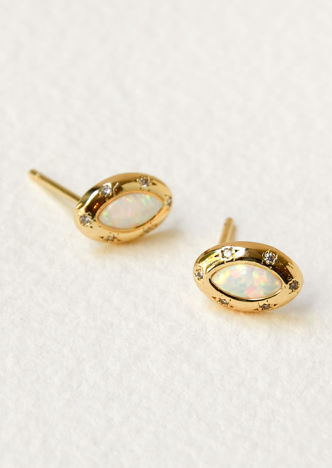 A pair of gold earrings with opals in the center surrounded by tiny cubic zirconia gems