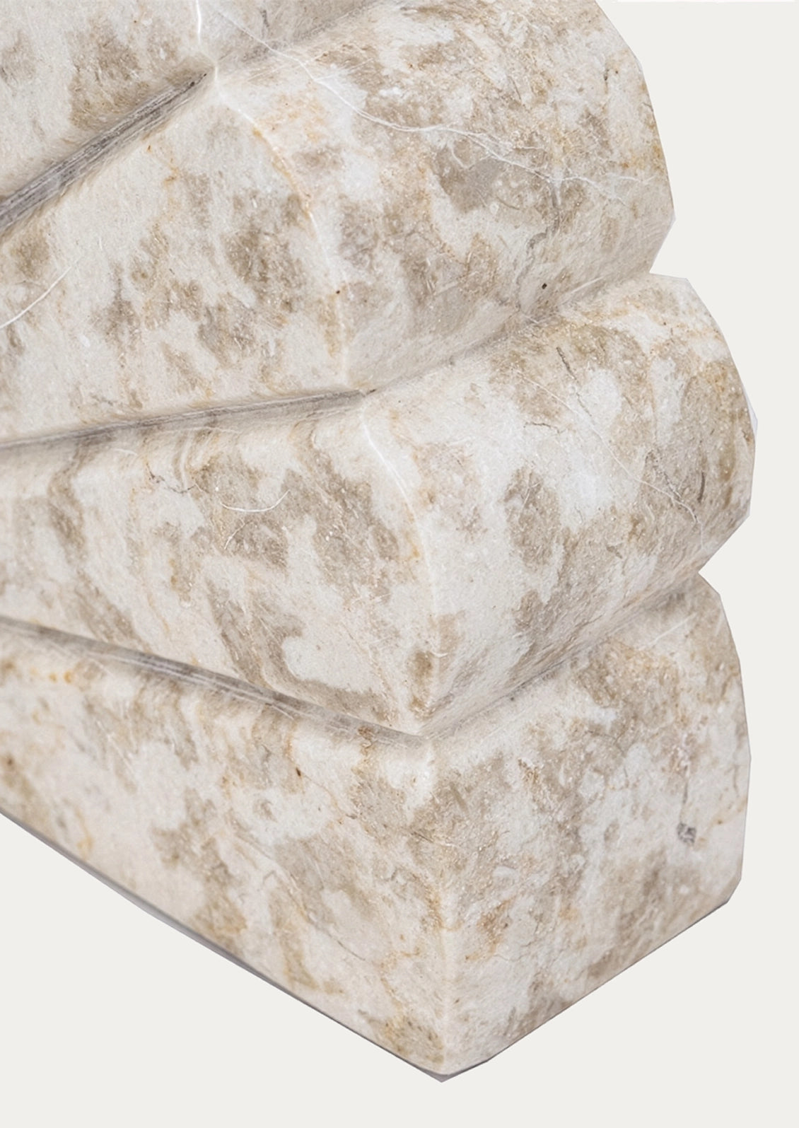 A close-up of a modern sculptural side table made from stacked, rounded stone blocks in a light beige and cream marbled pattern, set against a plain off-white background.