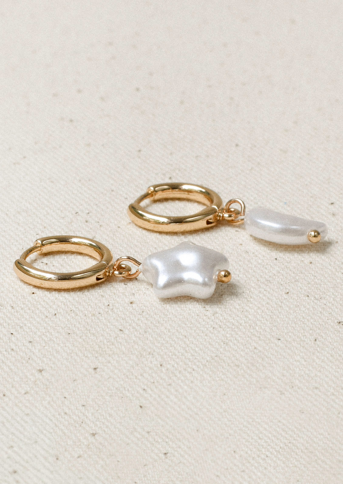 A pair of gold hoop earrings with large star and moon-shaped faux pearl charms.