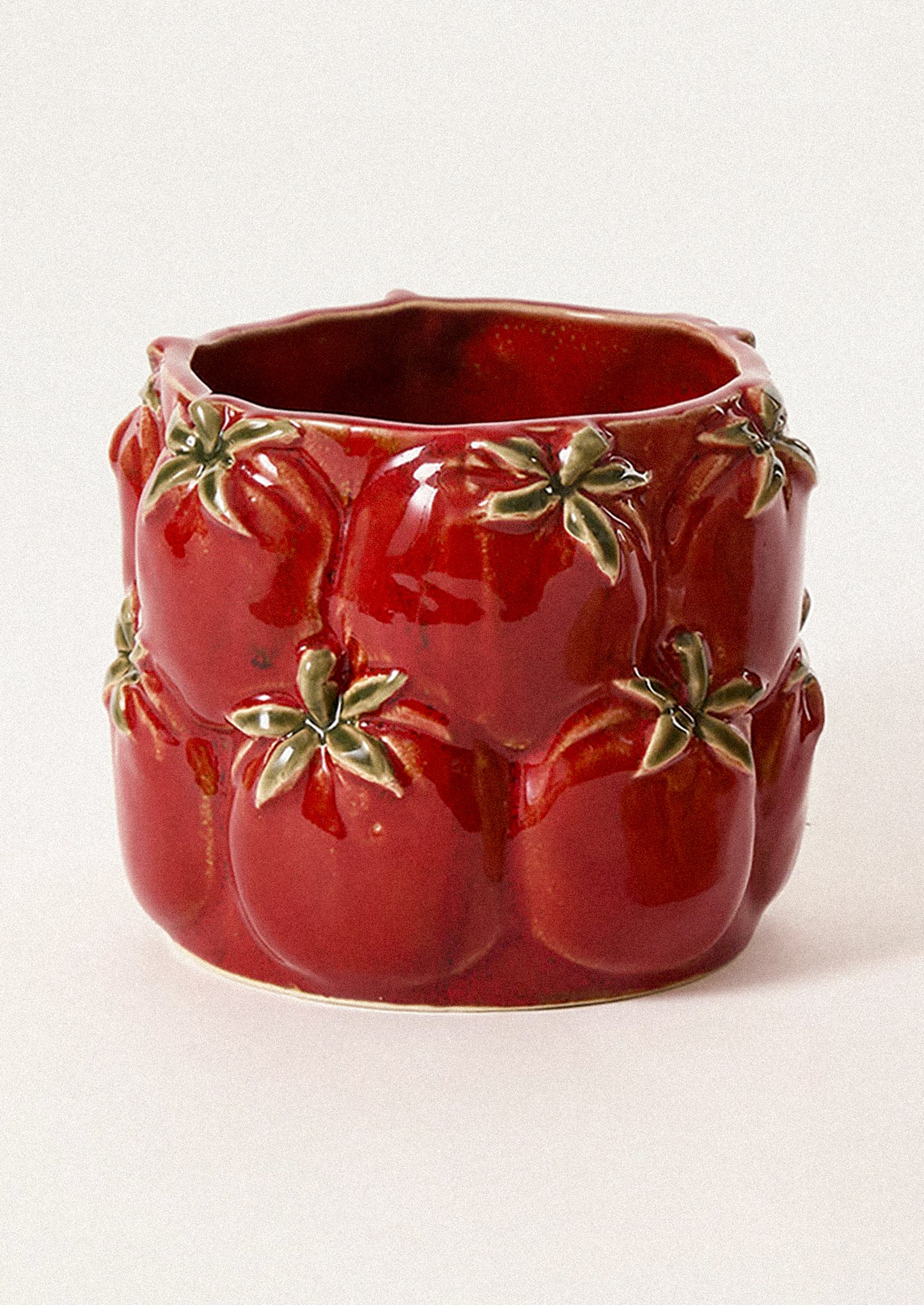 A glossy red ceramic planter shaped like a cluster of tomatoes, featuring raised tomato forms with green leafy tops.