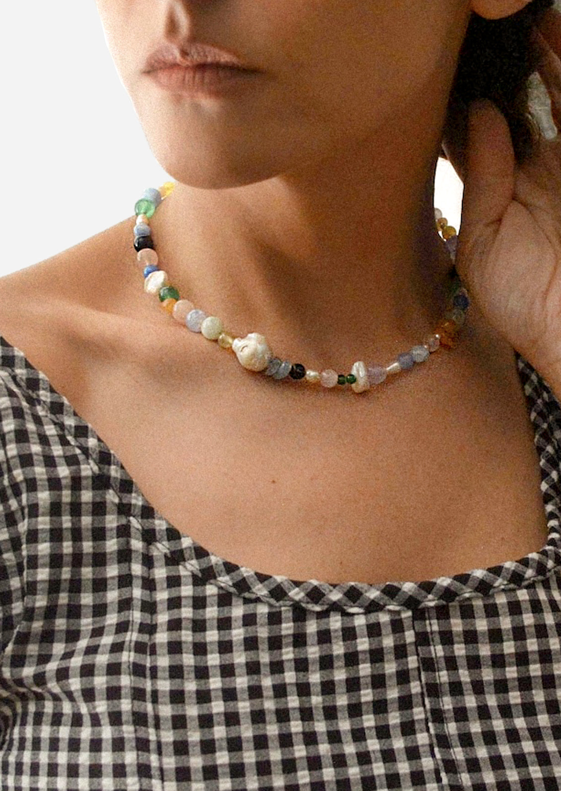 A woman wearing a necklace with colorful natural gemstones and baroque pearls.