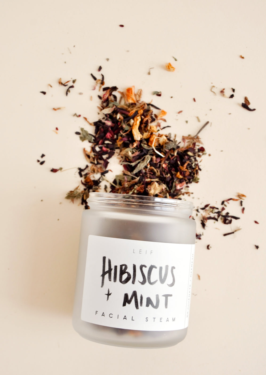 A small frosted glass jar with a black and white label spilling out a mix of dried flowers.