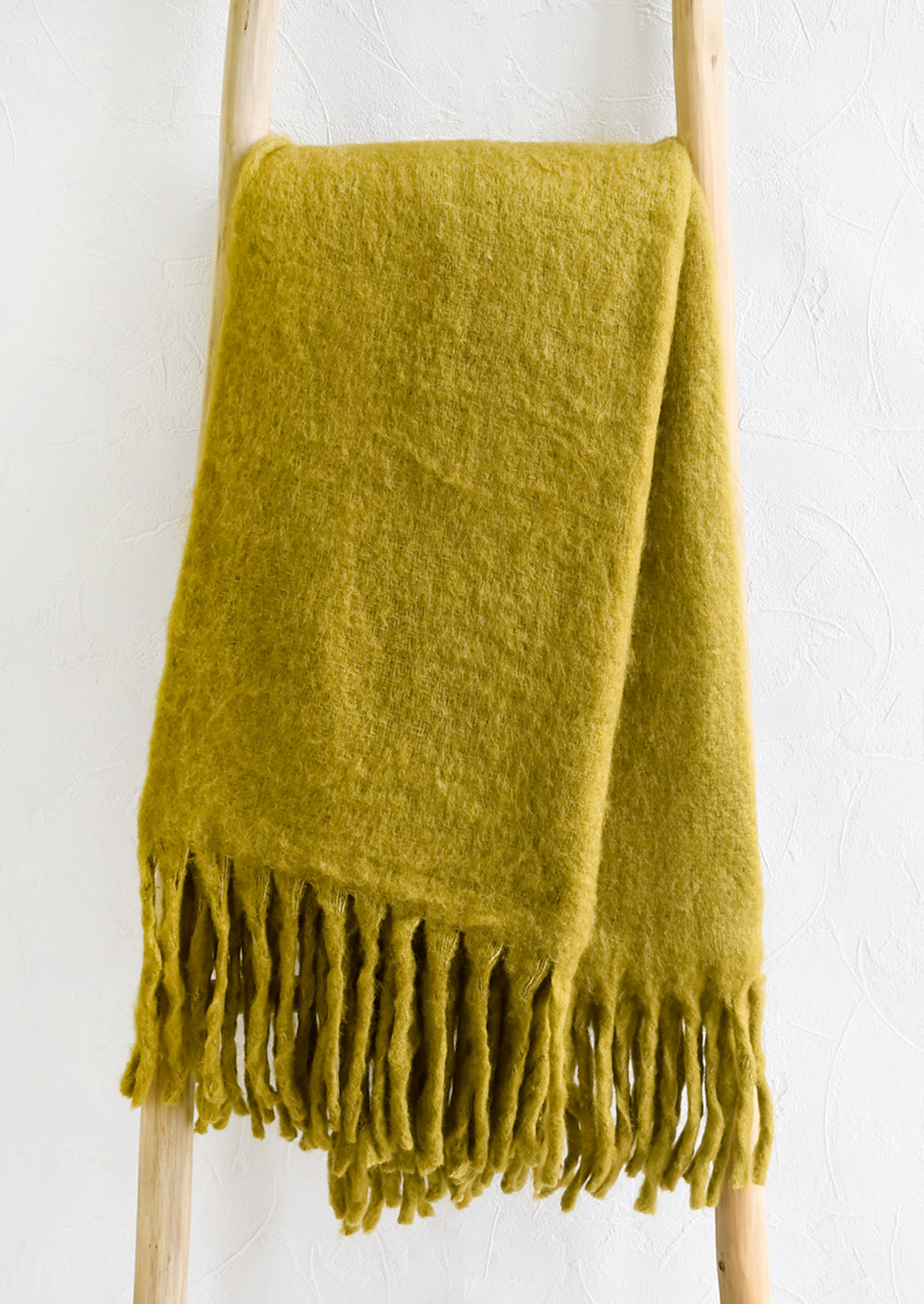 A chartreuse mohair blanket with long tassel fringe displayed on a ladder.