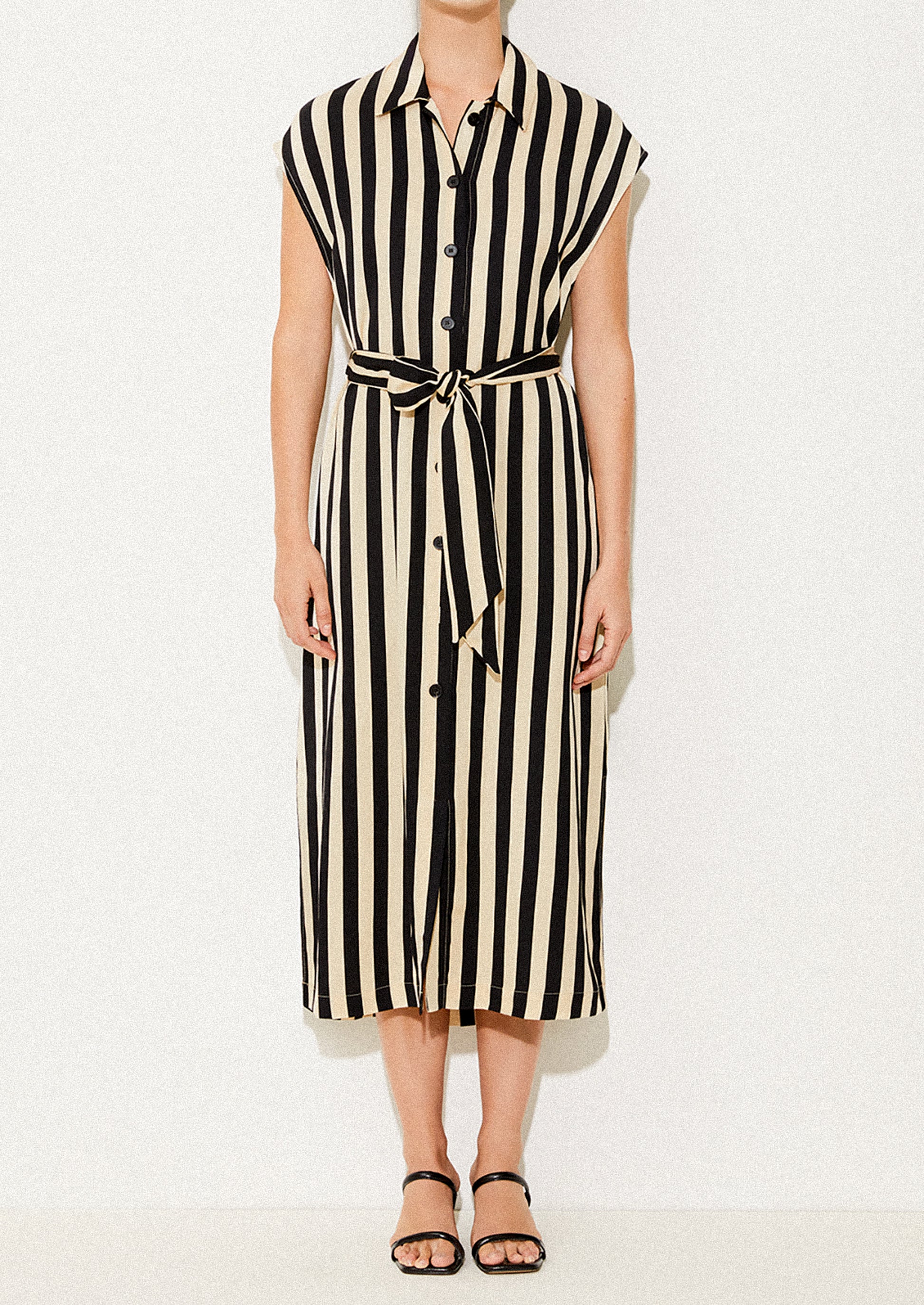 A woman wearing a sleeveless collared dress in vertical black and ivory stripes.