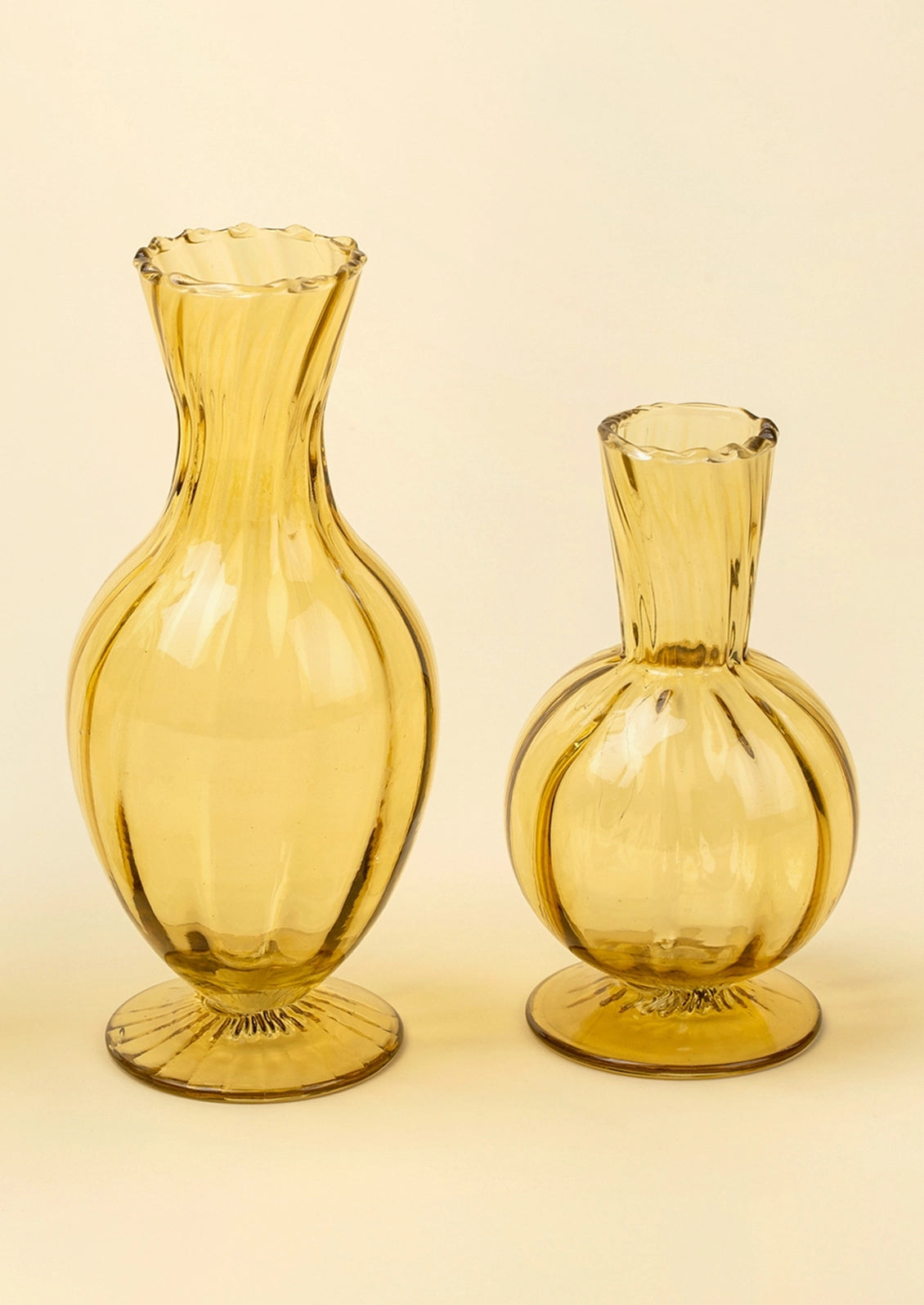 Two amber yellow glass vases with ribbed textures, one tall and one short, standing on a light beige background.