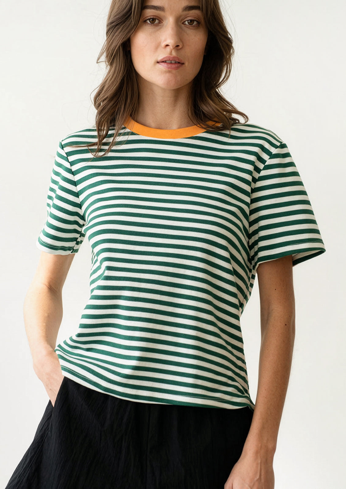 A woman wearing a short sleeve t-shirt in green and white stripes with orange neck trim.
