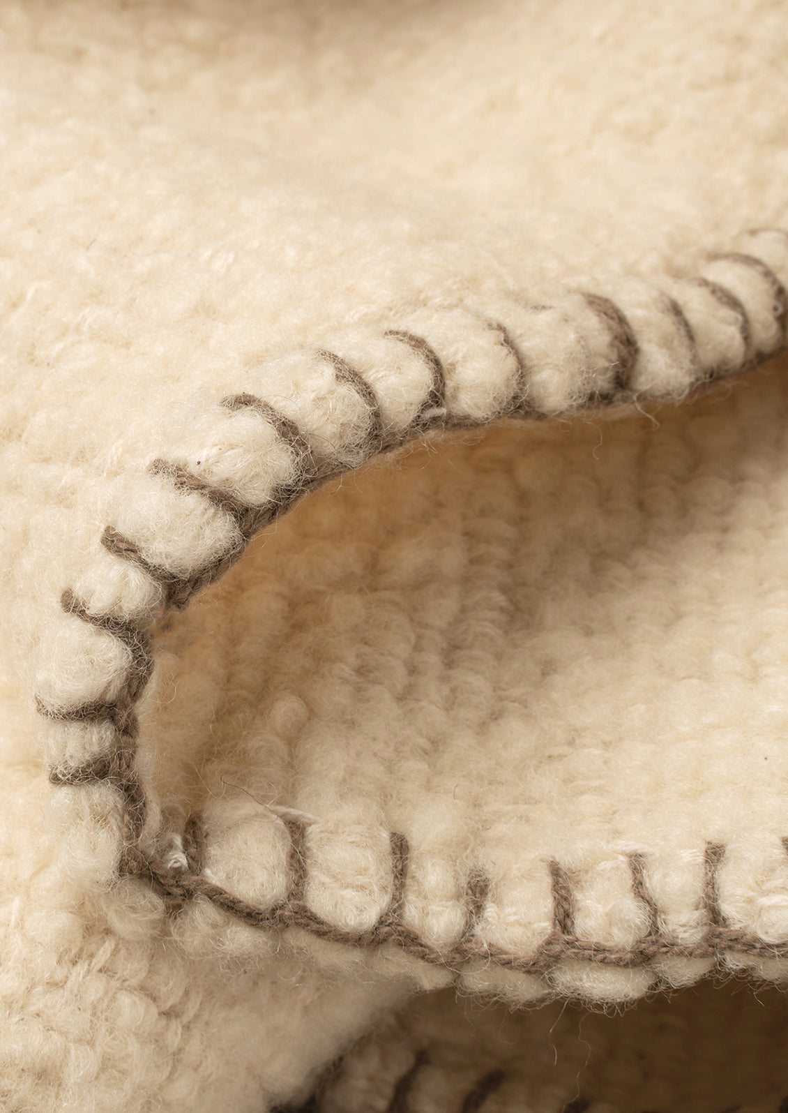 Close-up of a cream-colored textured fabric, folded over to show a stitched edge in a warm beige tone.