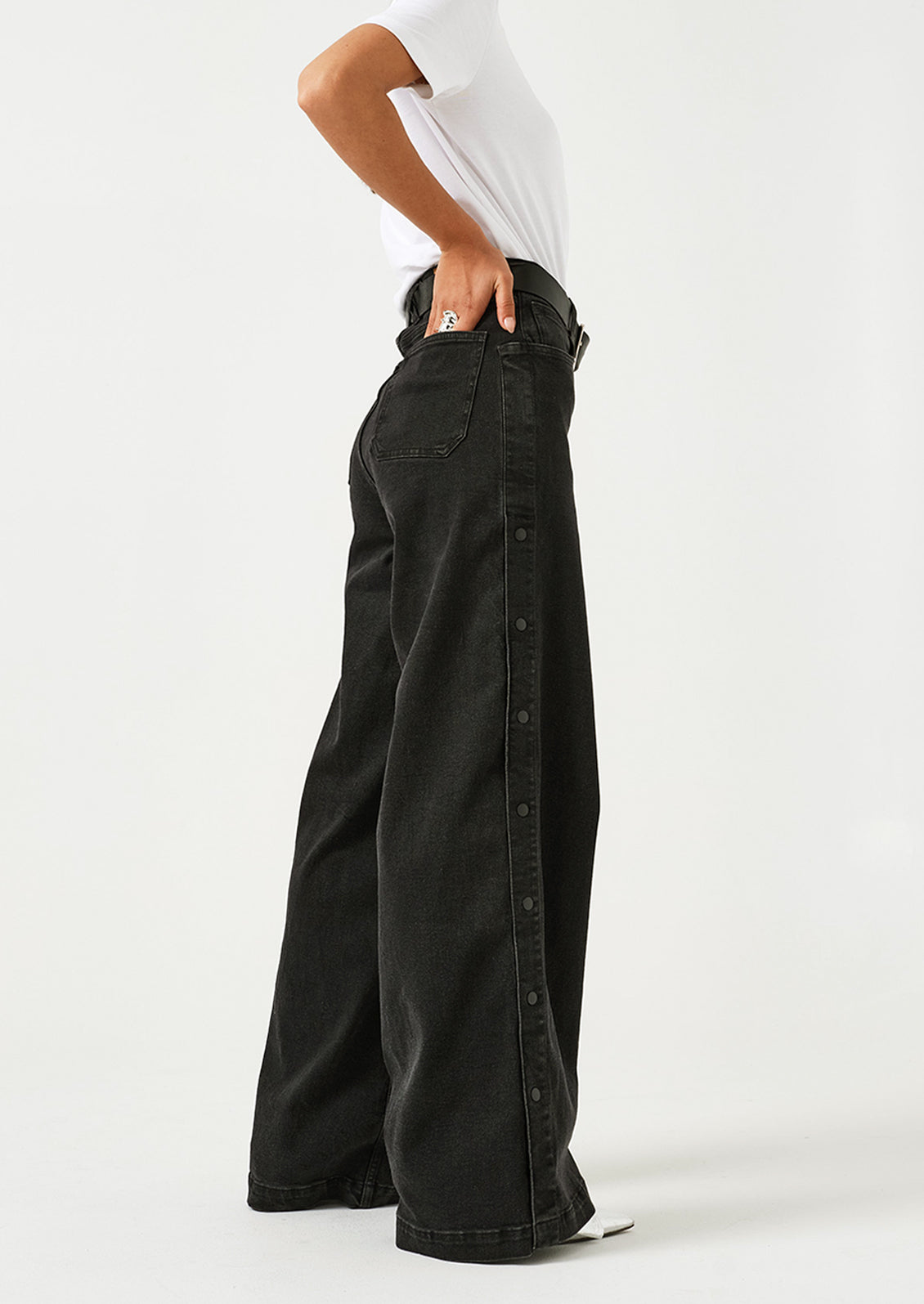 A woman wearing a pair of black wide leg jeans with windbreaker-style snap detail along outer leg.