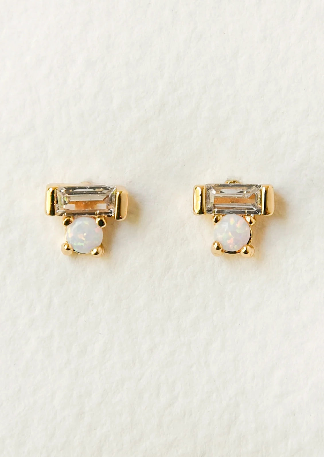 A pair of gold earrings with a baguette shaped gem stacked on top of an opal gem.