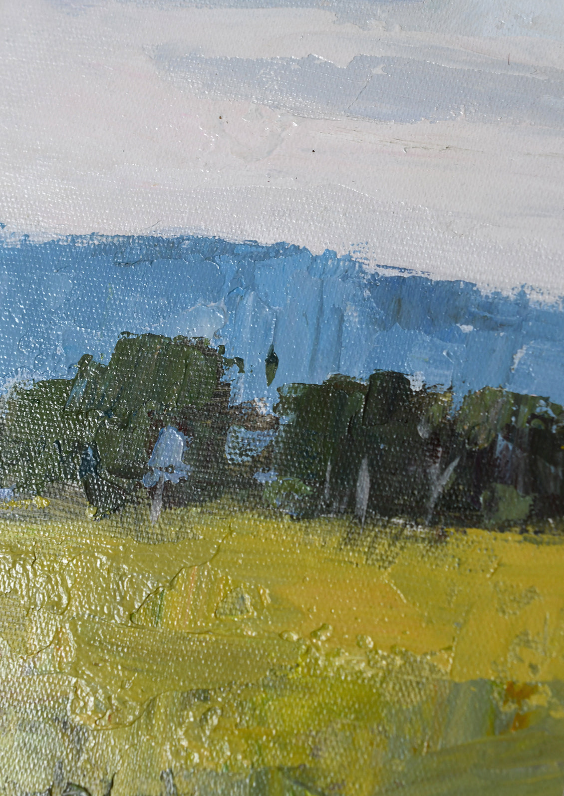 Impressionistic landscape painting featuring a bright yellow field in the foreground, dark green trees, and a blue mountain range under a pale gray sky.