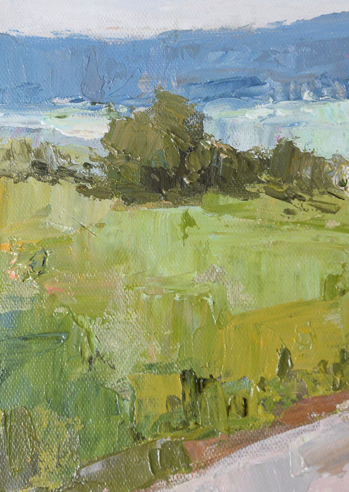 An impressionistic landscape painting featuring a vibrant green field in the foreground with dark green trees, blue mountains in the background, and a pale sky.