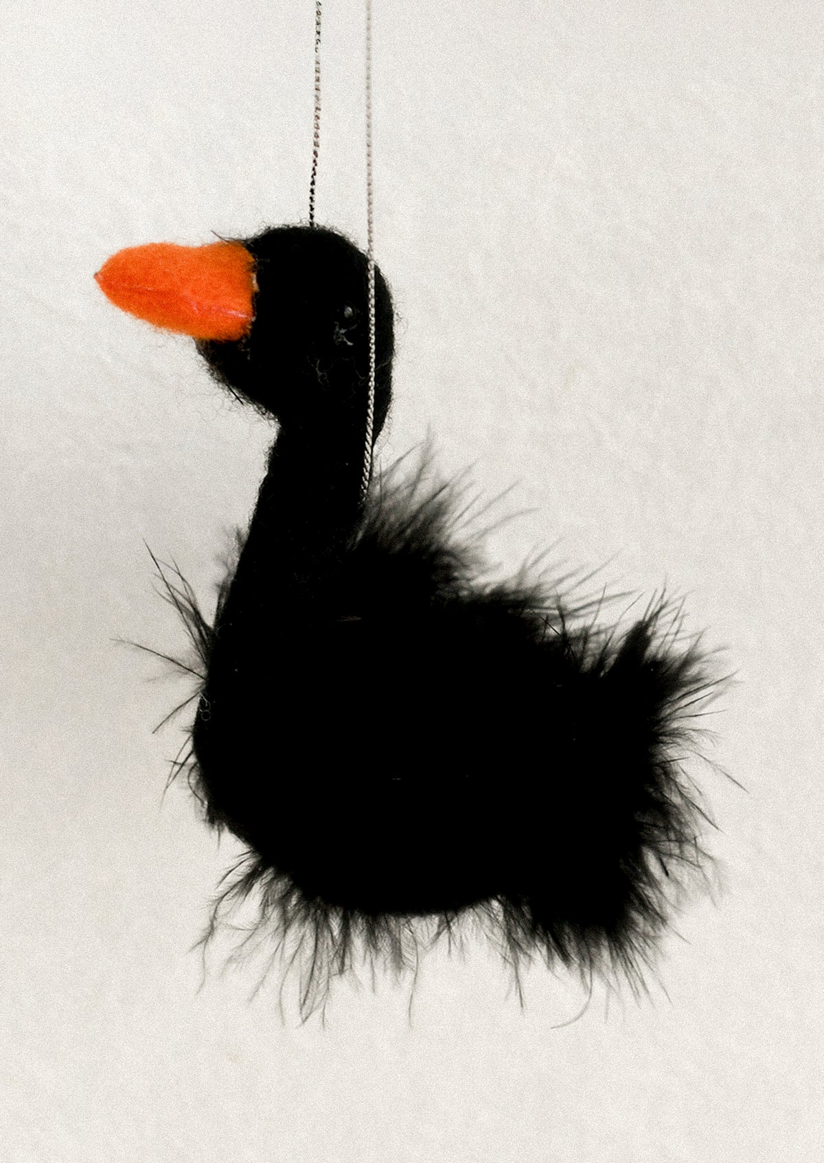 A black fluffy bird-shaped hanging ornament with a bright orange beak.