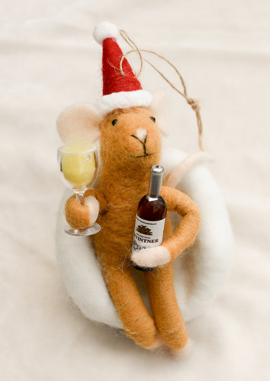 A felted ornament of a mouse sitting in a chair wearing santa hat, drinking wine.