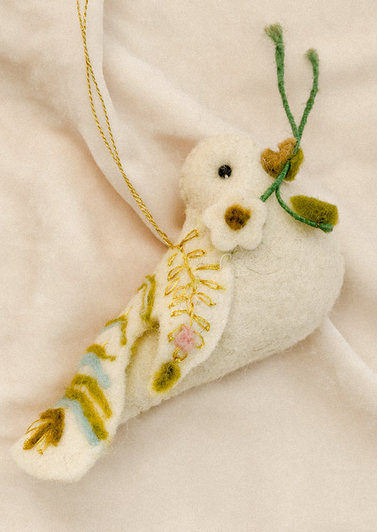 A felted white ornament depicting a dove holding a sprig in its beak, with decorative pastel embroidery.