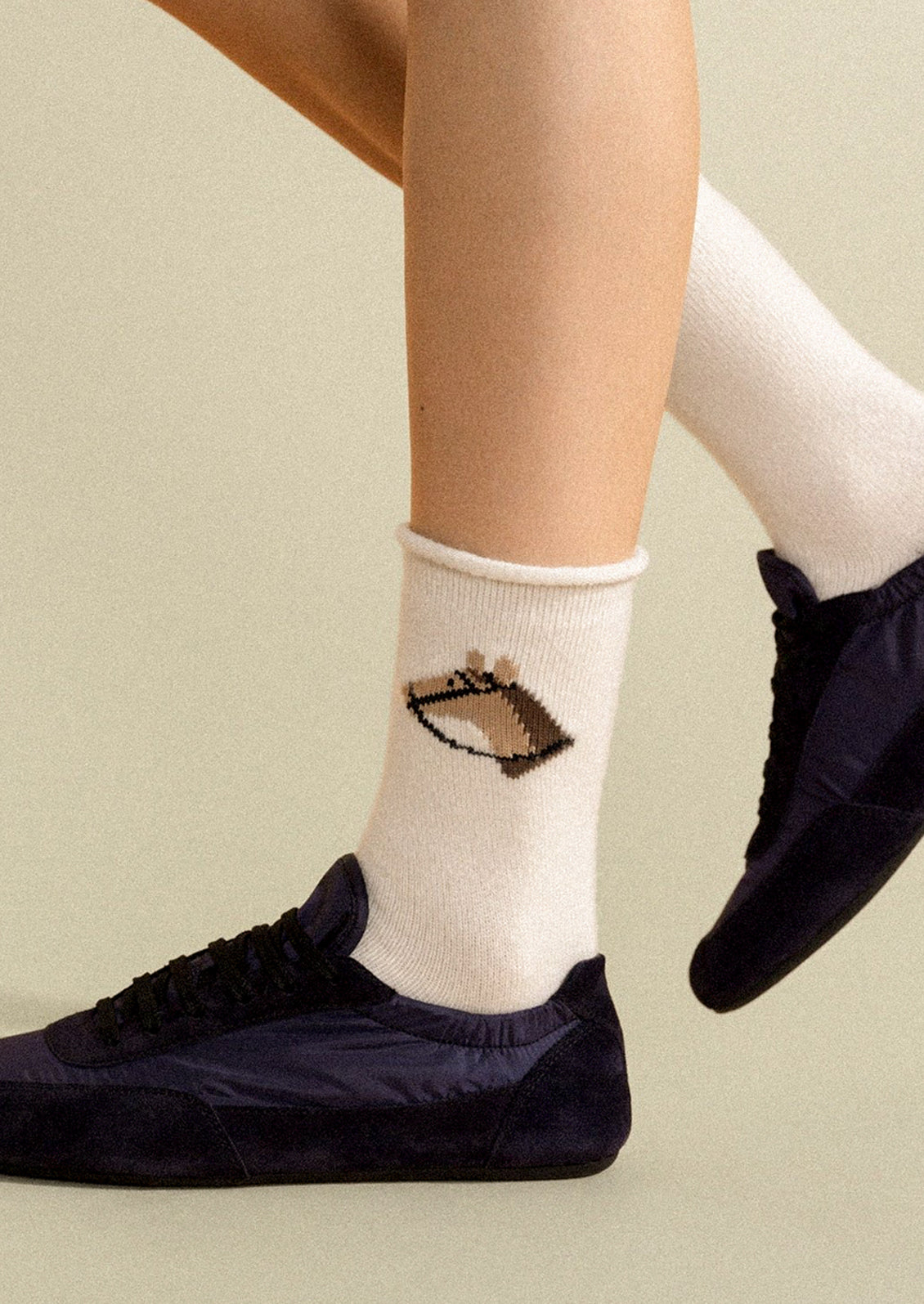 A person wearing ivory crew socks with a brown horse on them.