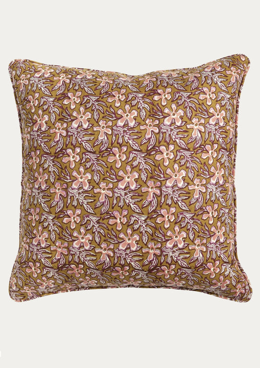 A square decorative throw pillow featuring an all-over floral block print pattern in pink and purple on a warm olive-brown background, shown against a plain light gray studio backdrop.