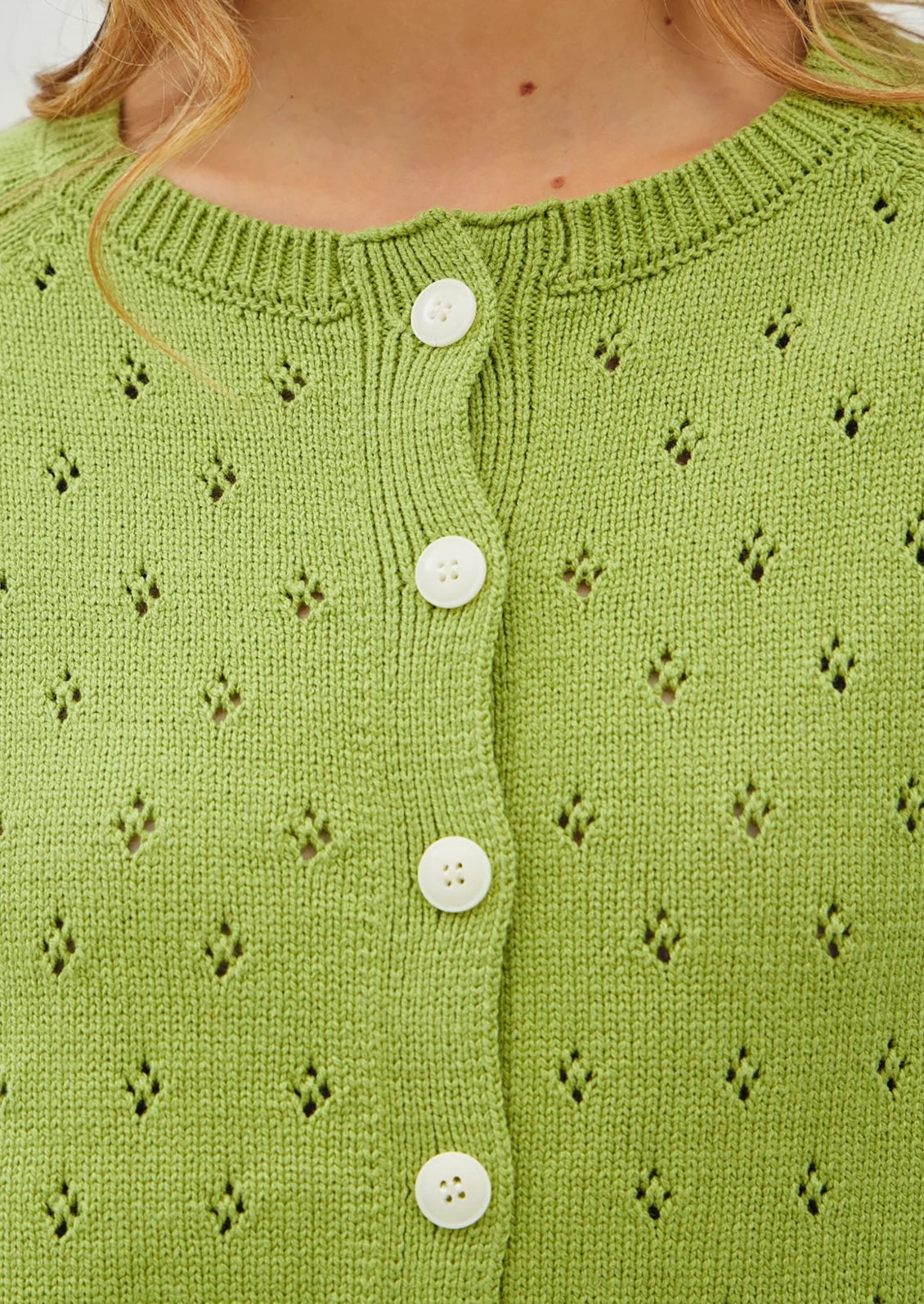 A woman wearing a light green knit cardigan sweater with white buttons.