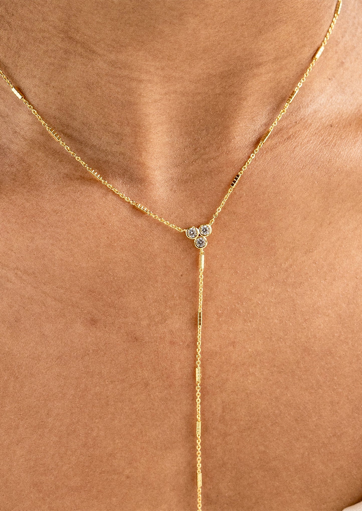 A close-up of a gold Y-necklace with a small three-stone floral cluster at the center, worn on a model's neck.