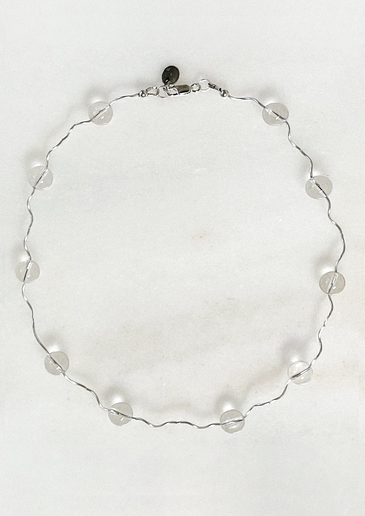 A necklace with a wavy sterling silver band adorned with clear round quartz stations.