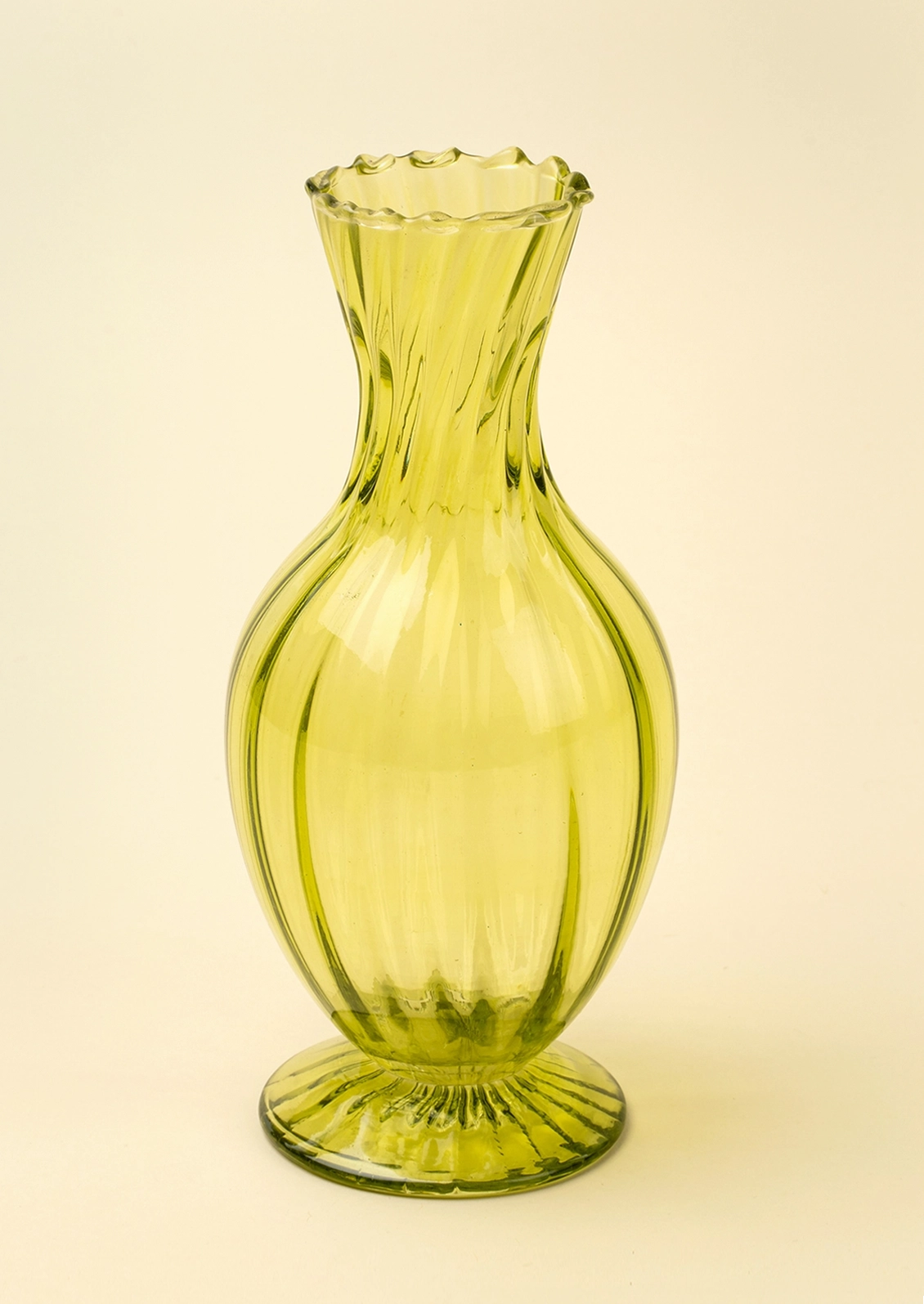 A translucent olive green glass vase with a flared, scalloped neck and a ribbed base, set against a solid cream background.