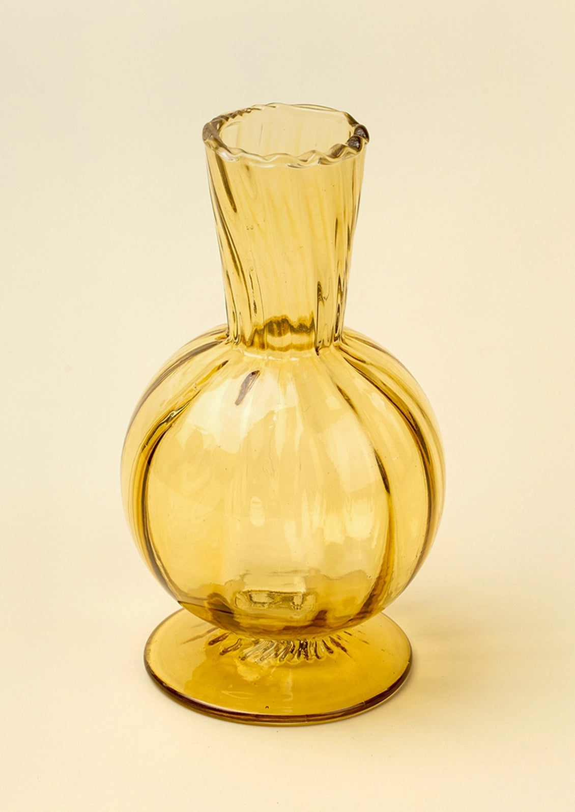 A translucent amber yellow glass vase with a bulbous rounded body, flared ribbed neck, and a small flared base, photographed on a plain warm off-white background.