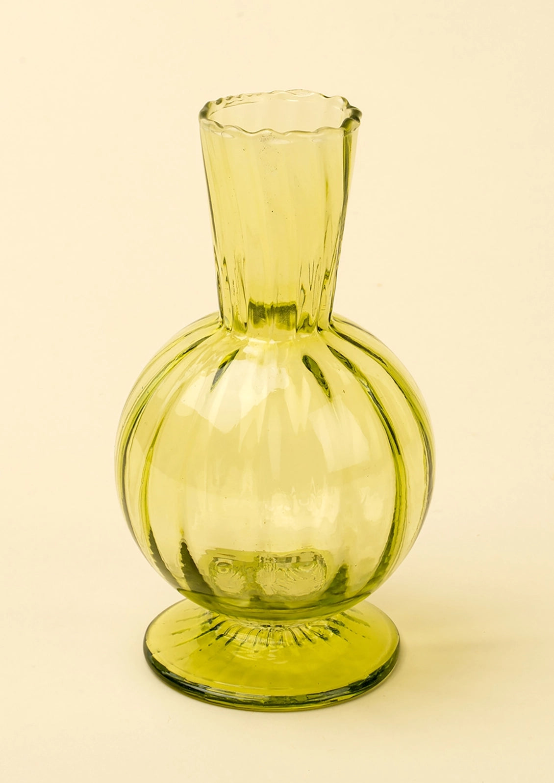A vintage-style translucent glass vase with a bulbous round body, narrow neck, and flared base in a pale yellow-green color, set against a solid cream background.