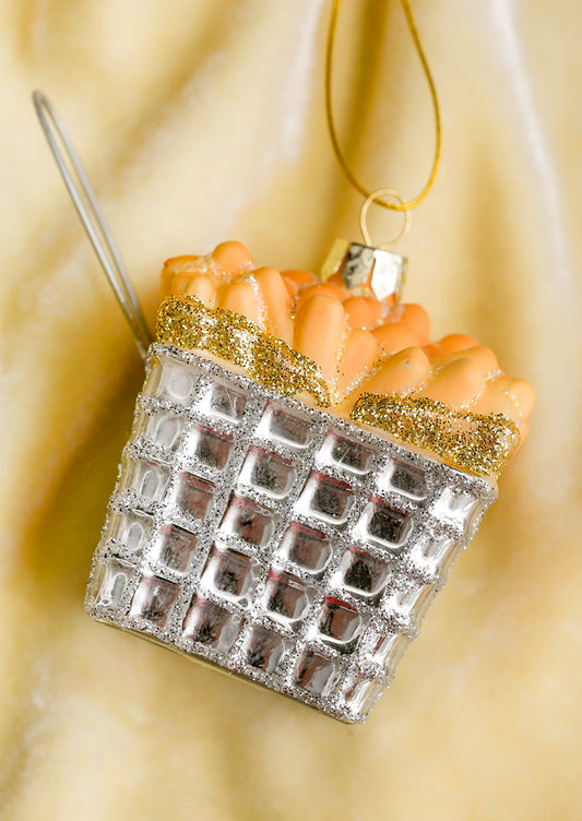 A glass ornament of french fries in a silver frying basket with handle.