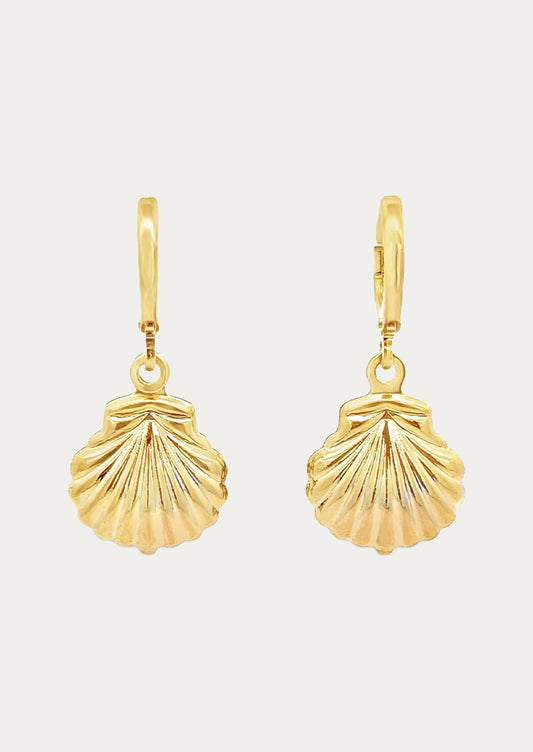 A pair of gold huggie hoop earrings with gold dangling seashell charms on a white background.