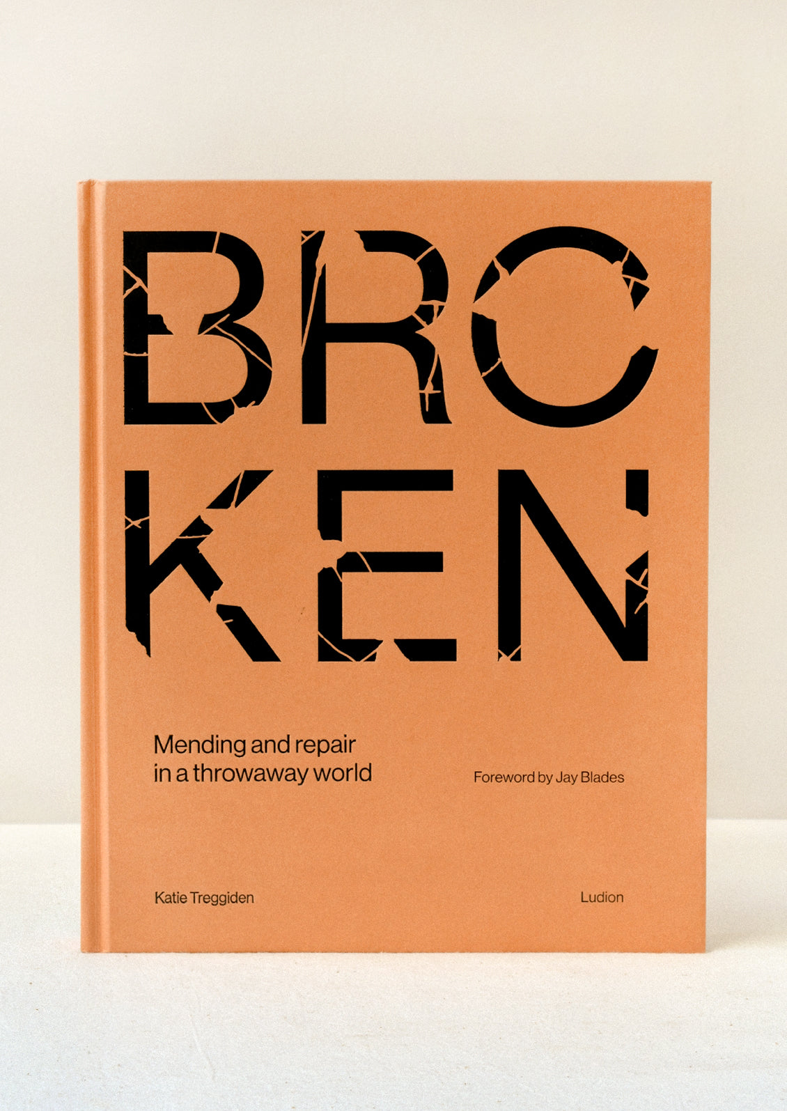 A hardcover orange book with the title "BROKEN" in large broken black letters standing upright on a table.