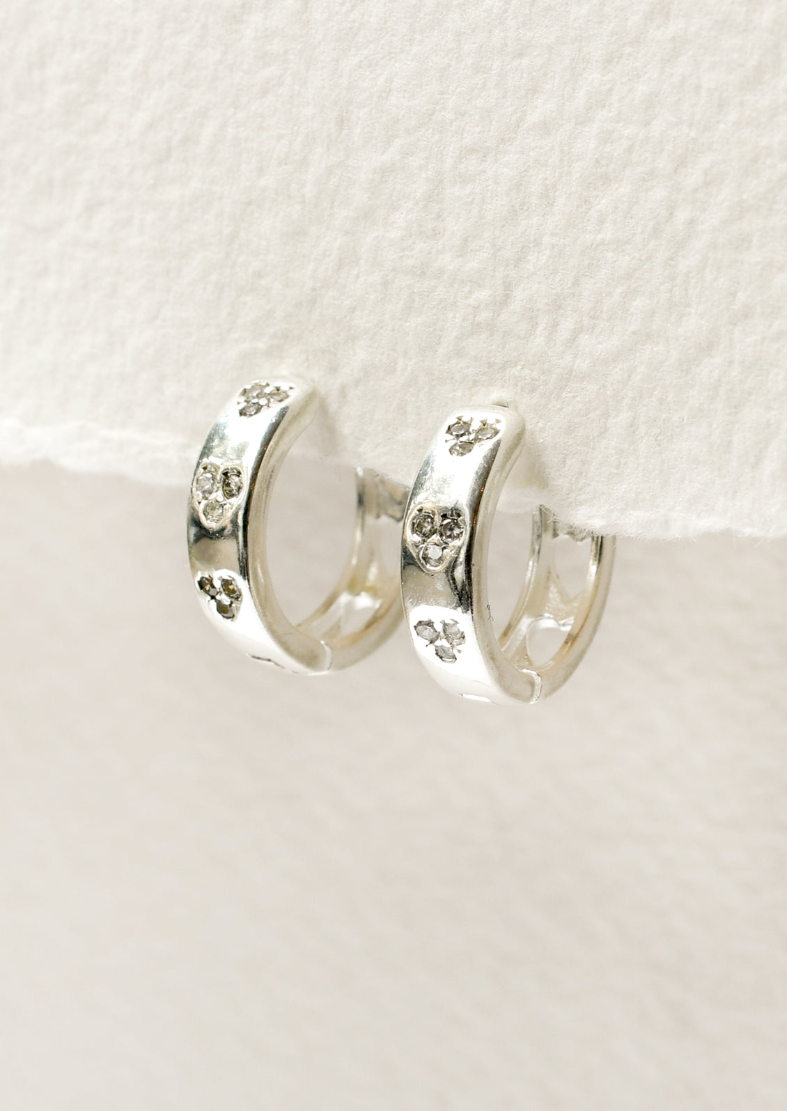 A pair of sterling silver huggie hoop earrings with heart-shaped holes on the back and crystal clusters on the front.