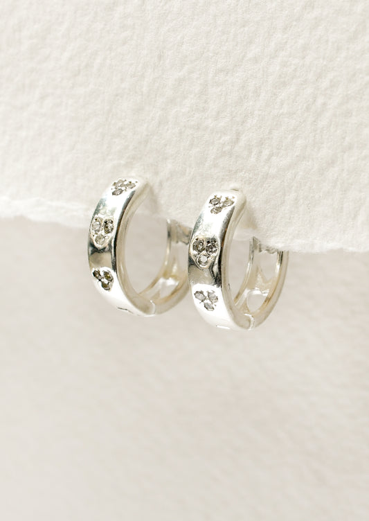 A pair of sterling silver huggie hoop earrings with heart-shaped holes on the back and crystal clusters on the front.