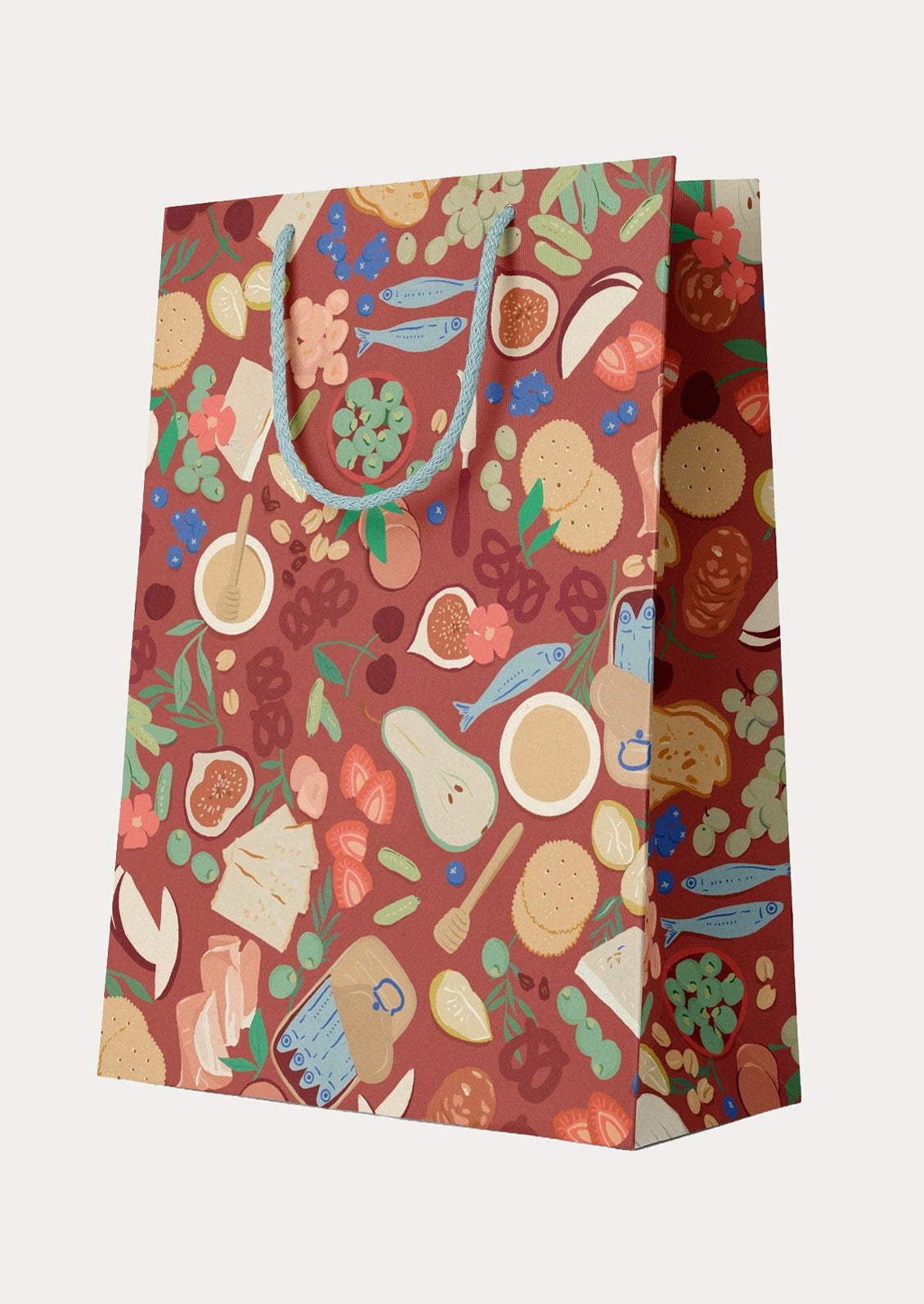 A printed gift bag with allover charcuterie foods print on rust colored background, with light blue rope handle.