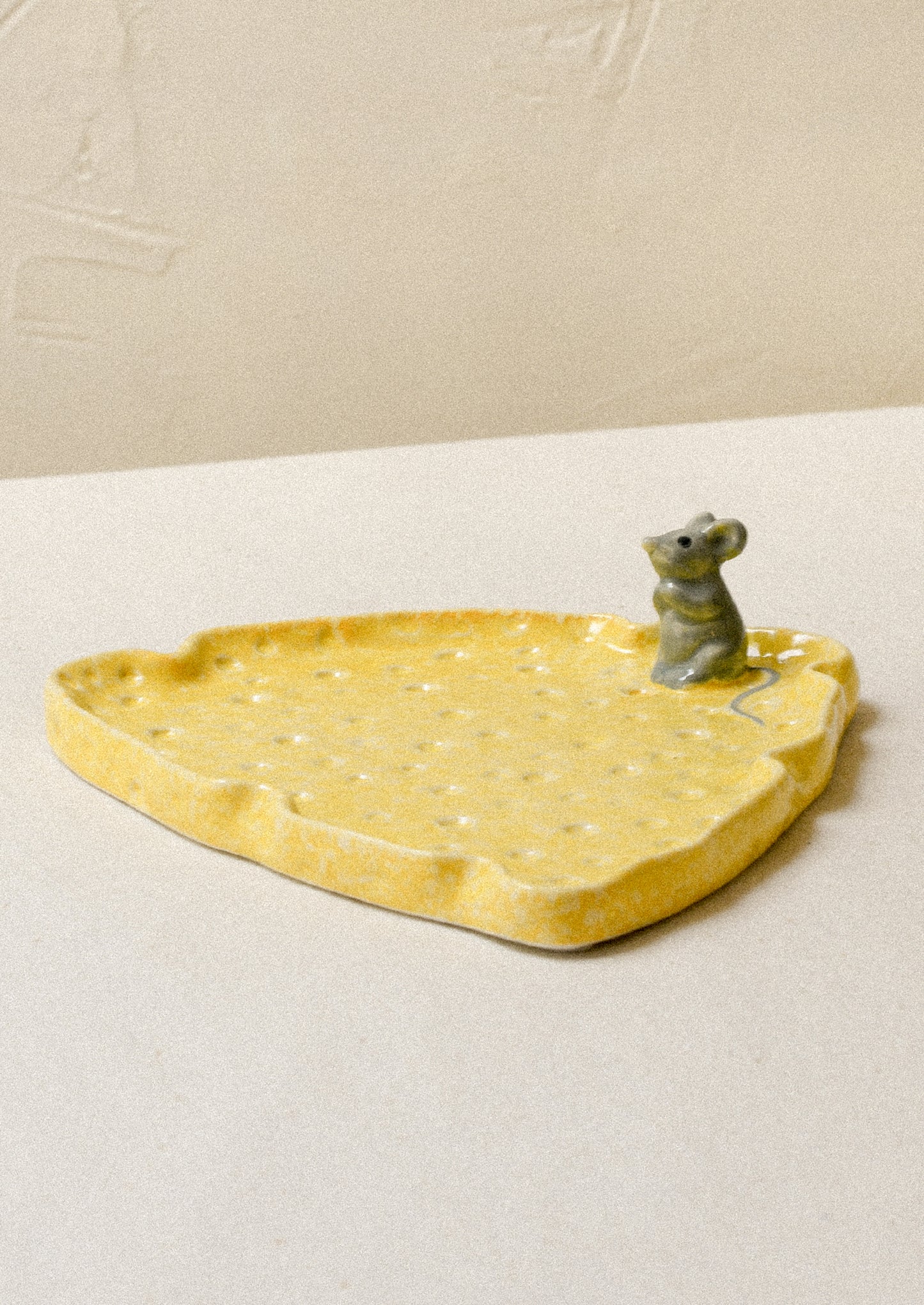 A ceramic plate in the shape of a slice of cheese with a mouse figurine on top.