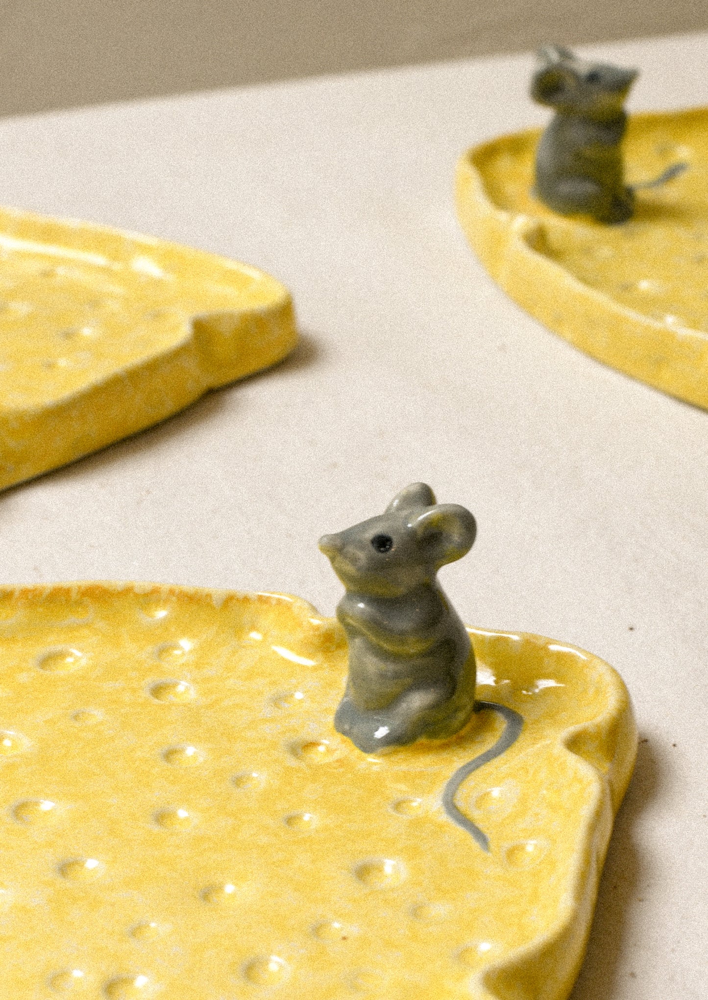 A ceramic plate in the shape of a slice of cheese with a mouse figurine on top.