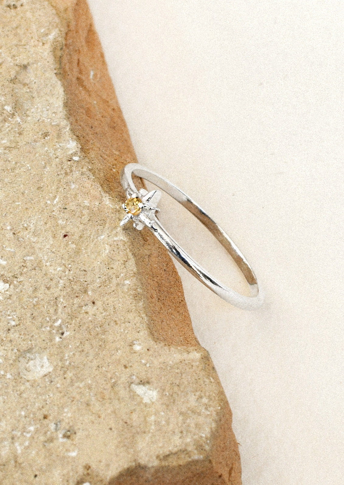 A sterling silver ring with a thin band and a citrine stone in the center set in a starburst design leaning on a brown stone.