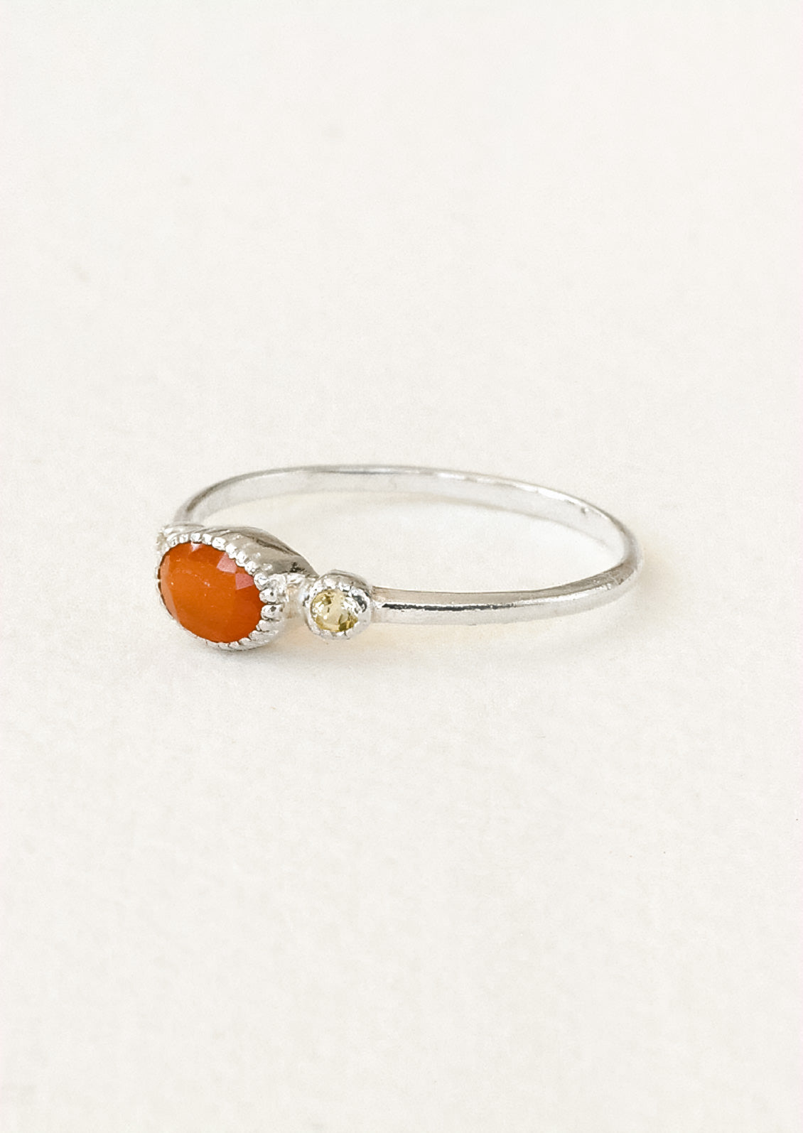Side view of a sterling silver ring with a carnelian oval in the center framed by two small round citrine stones on either side.