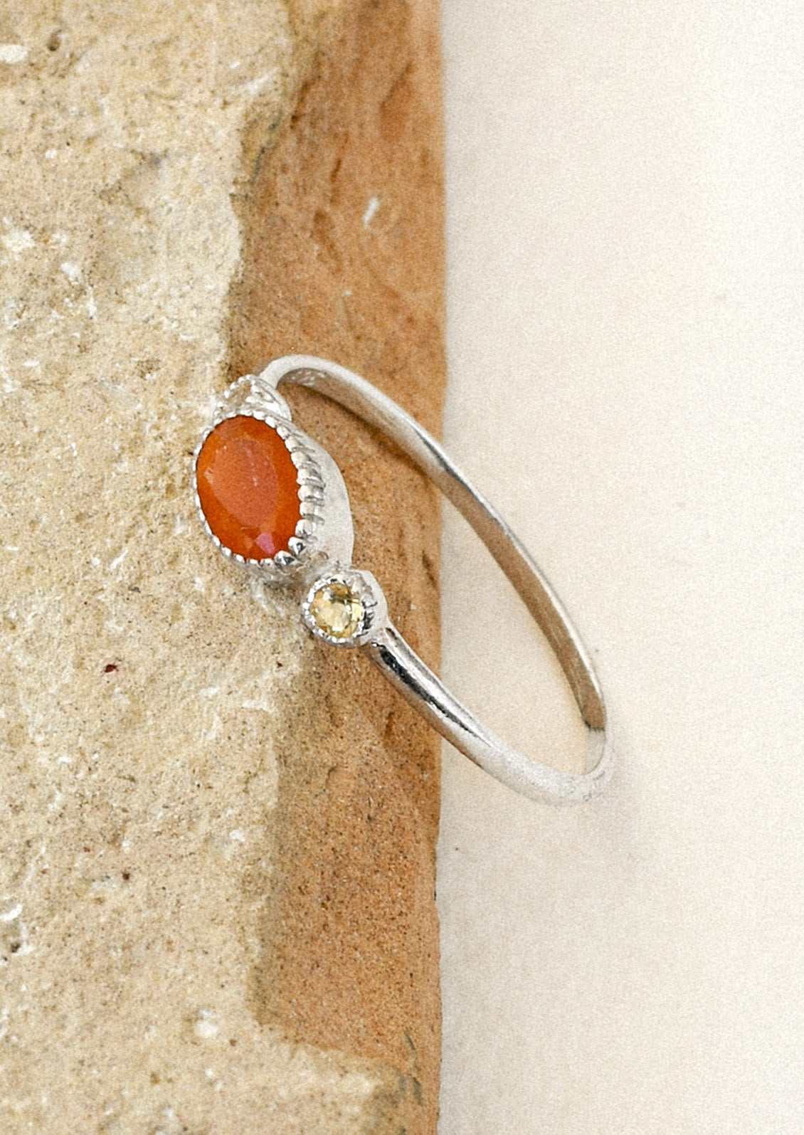 A sterling silver ring with a carnelian oval in the center framed by two small round citrine stones on either side leaning on s brown stone.