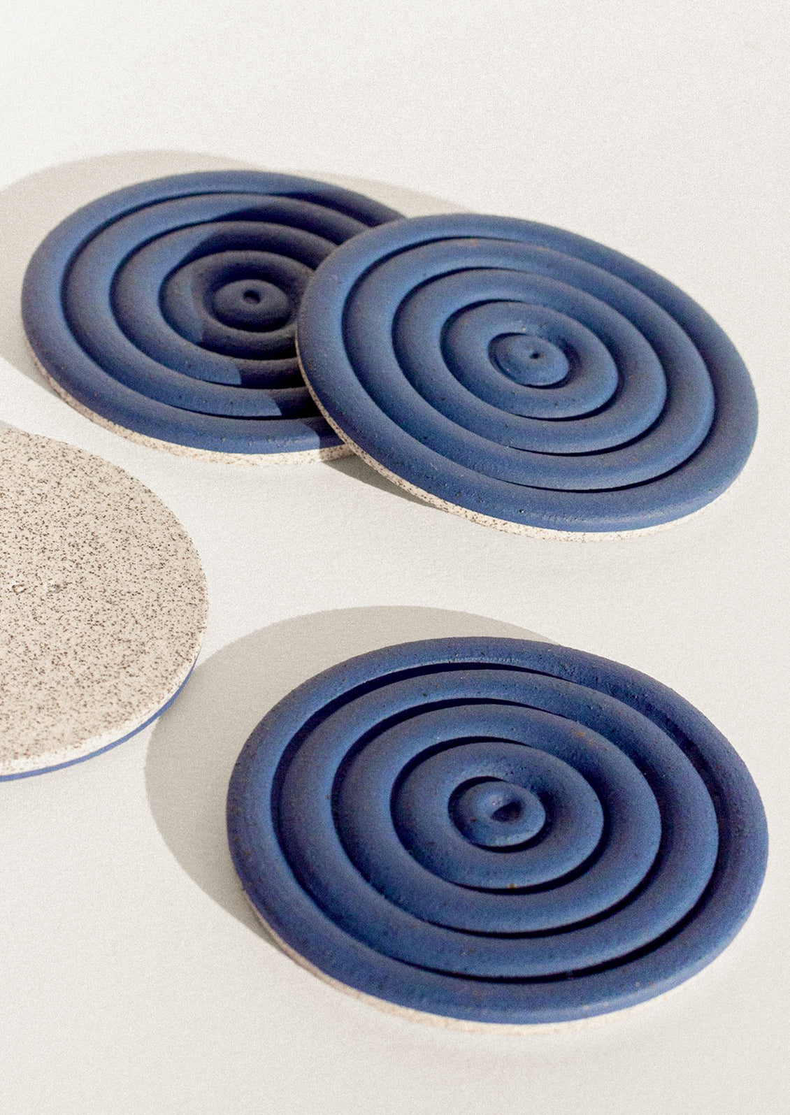 Handmade speckled ceramic coasters with a concentric design in cobalt blue.
