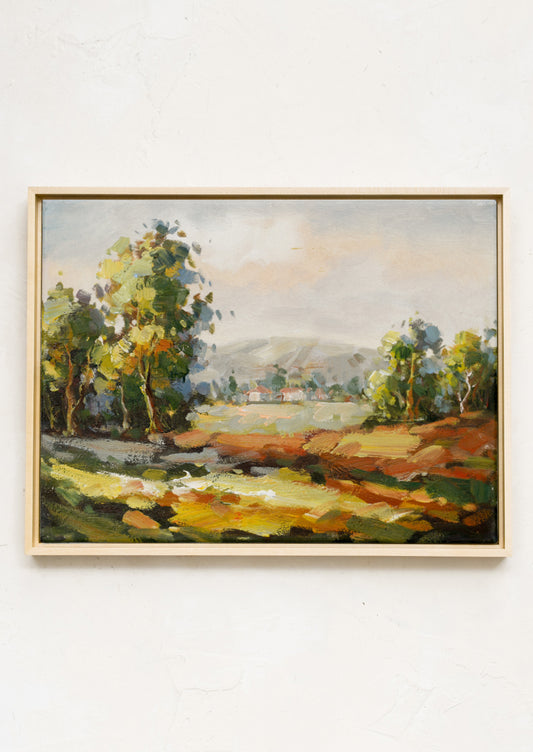 A framed original landscape oil painting of the countryside with houses in the distance.
