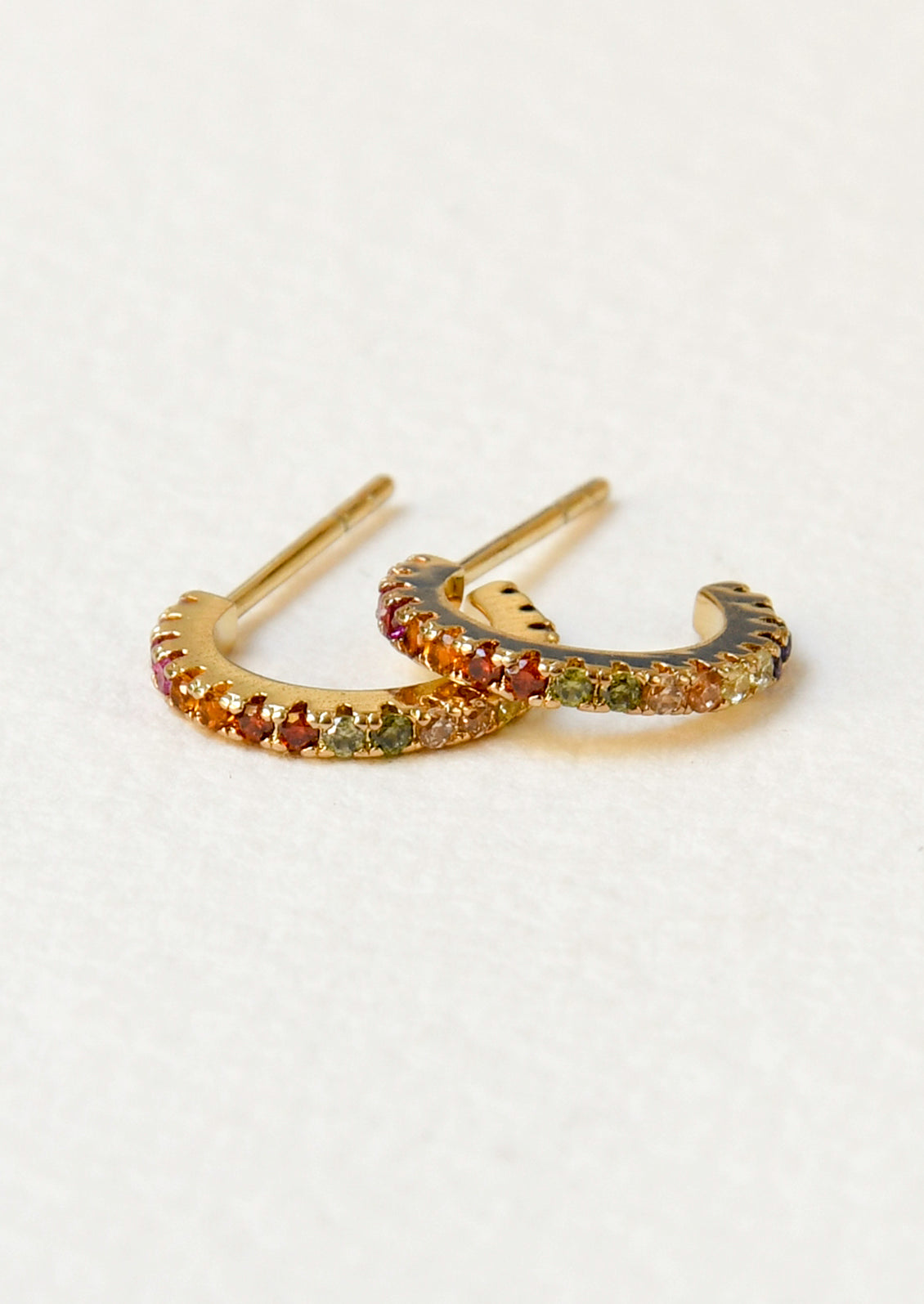 A pair of gold hoop earrings with pink, range, red, green, and clear gems in a gradient design.