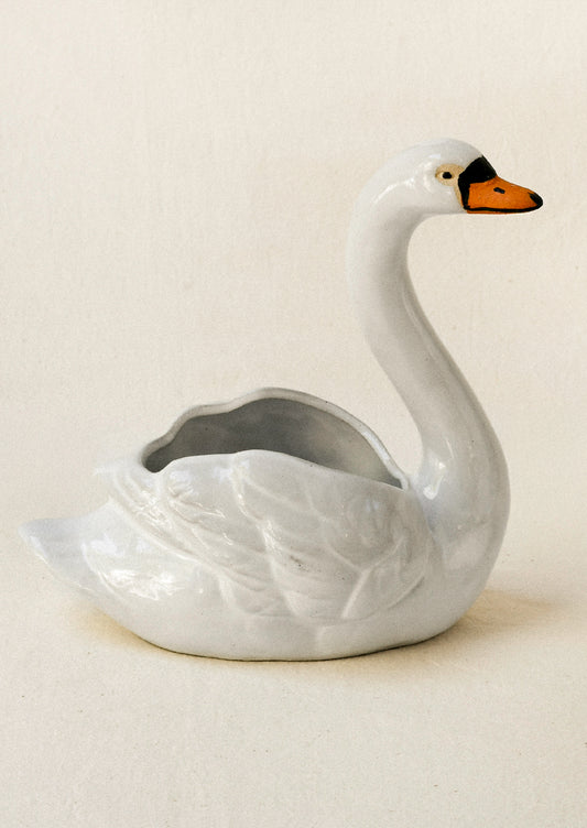 A ceramic planter in the shape of a cygnet sitting atop a table against a beige backdrop.