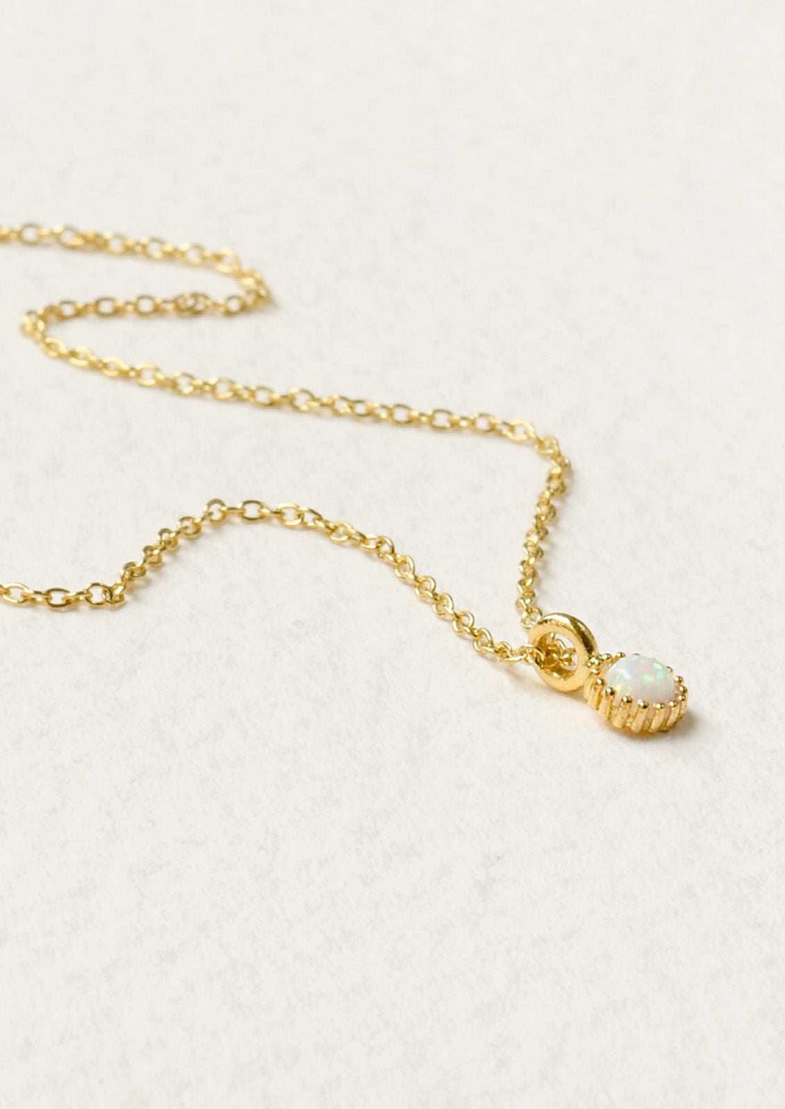 A dainty gold necklace with a small simulated opal charm.
